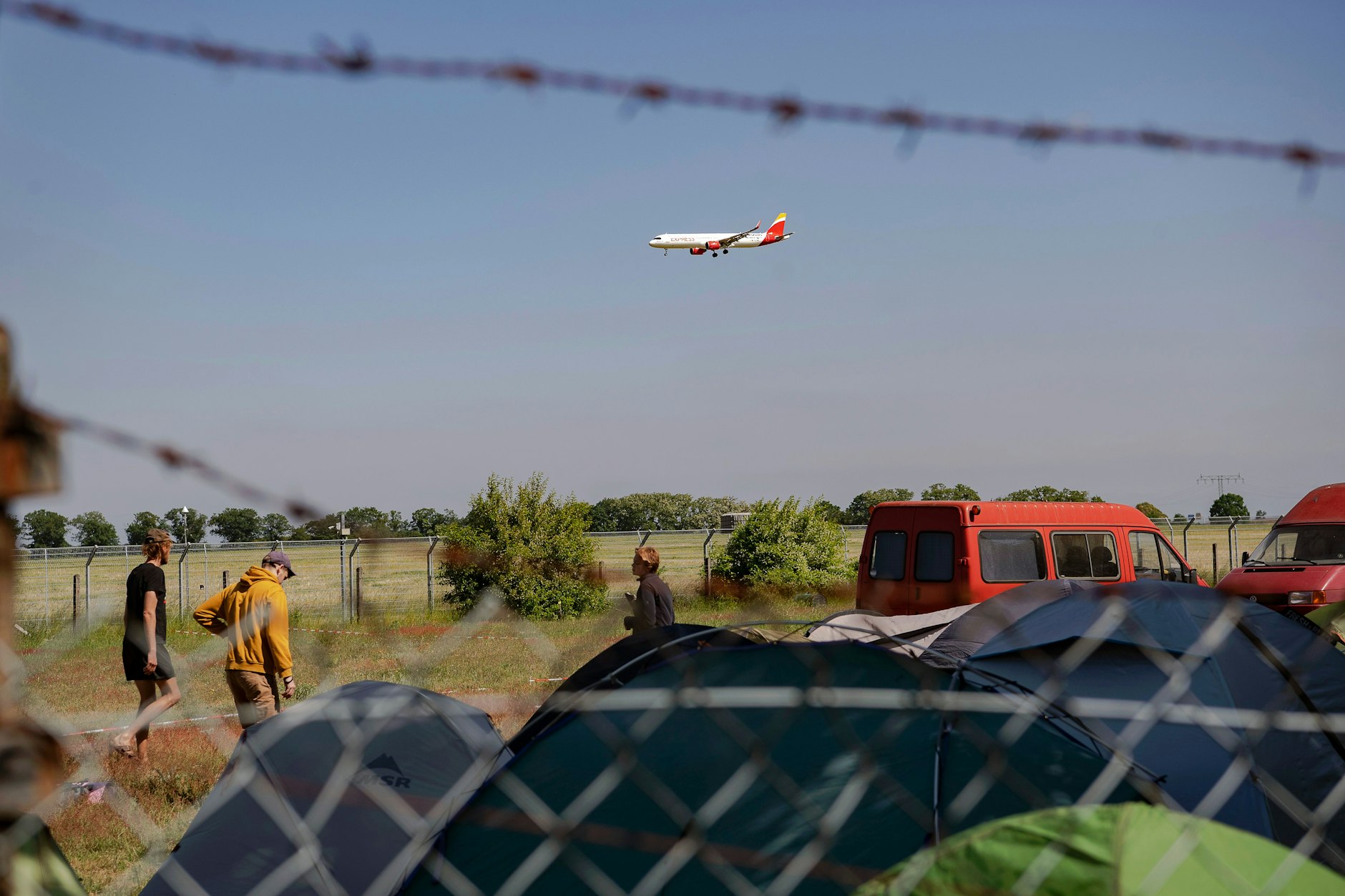 Schönefeld: Teilnehmer am Protestcamp der Initiative „Abschiebezentrum BER verhindern“ bauen ihre Zelte auf, während über ihnen ein Flugzeug fliegt.