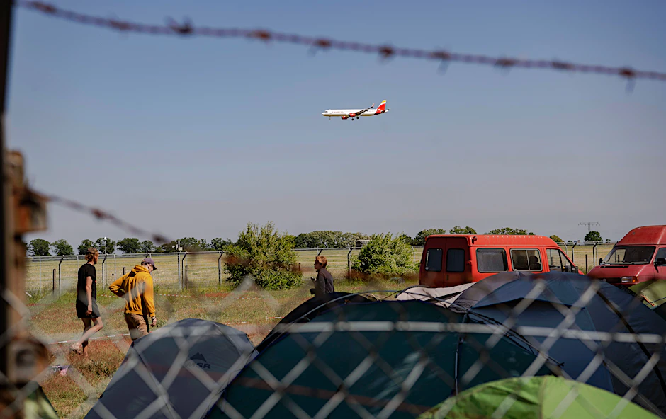Schönefeld: Teilnehmer am Protestcamp der Initiative „Abschiebezentrum BER verhindern“ bauen ihre Zelte auf, während über ihnen ein Flugzeug fliegt.