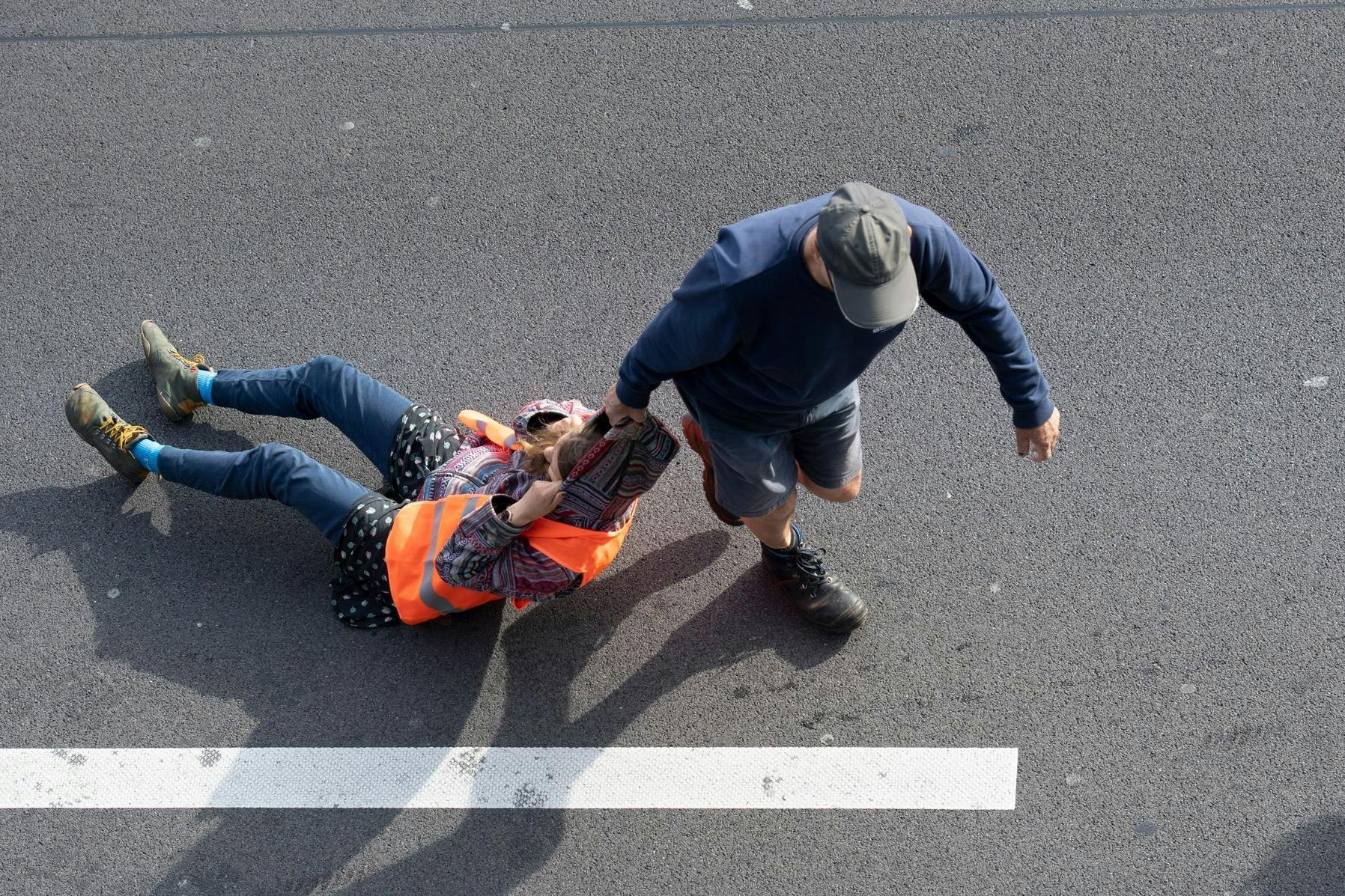 Ein Verkehrsteilnehmer (r.) zieht bei einer Blockade der Letzten Generation auf der Autobahn 100 eine Aktivistin (l.) von der Straße.