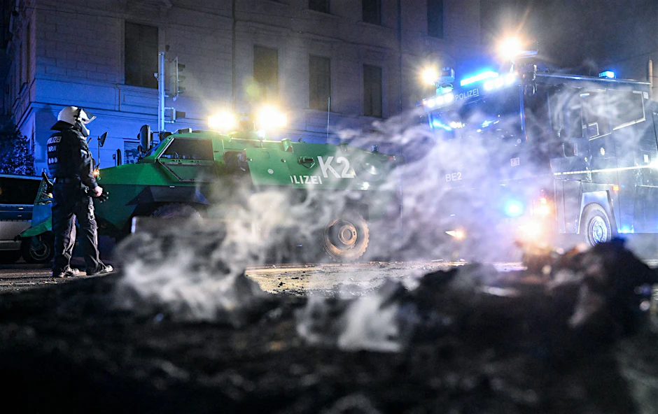 Polizisten stehen hinter einer rauchenden Barrikade im Stadtteil Connewitz in Leipzig.  