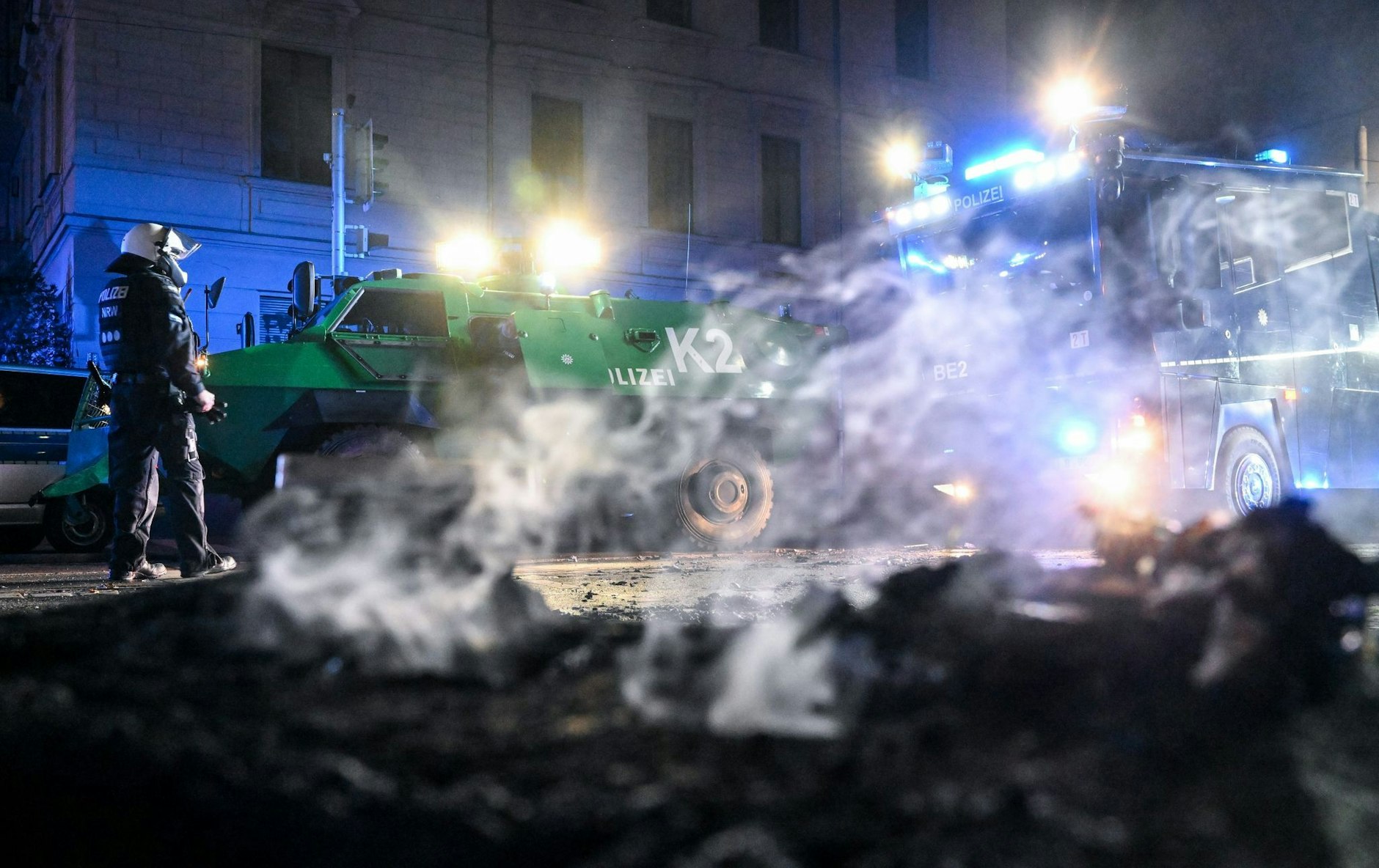 Polizisten stehen hinter einer rauchenden Barrikade im Stadtteil Connewitz in Leipzig.  