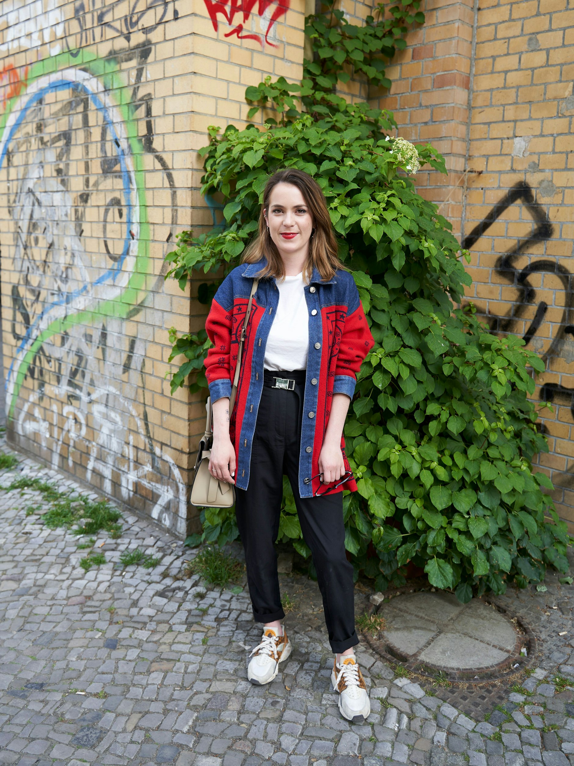 Katrins absolviert ihren Berlinbesuch in einem Cardigan-Jeansjacken-Hybrid von Sandro. Darunter trägt sie Basics von Tally Weijl, Nike Air Huarache und eine Karl-Lagerfeld-Tasche. Weil sie roten Lippenstift liebt, wie sie erzählt, darf der selbstverständlich auch heute nicht fehlen.