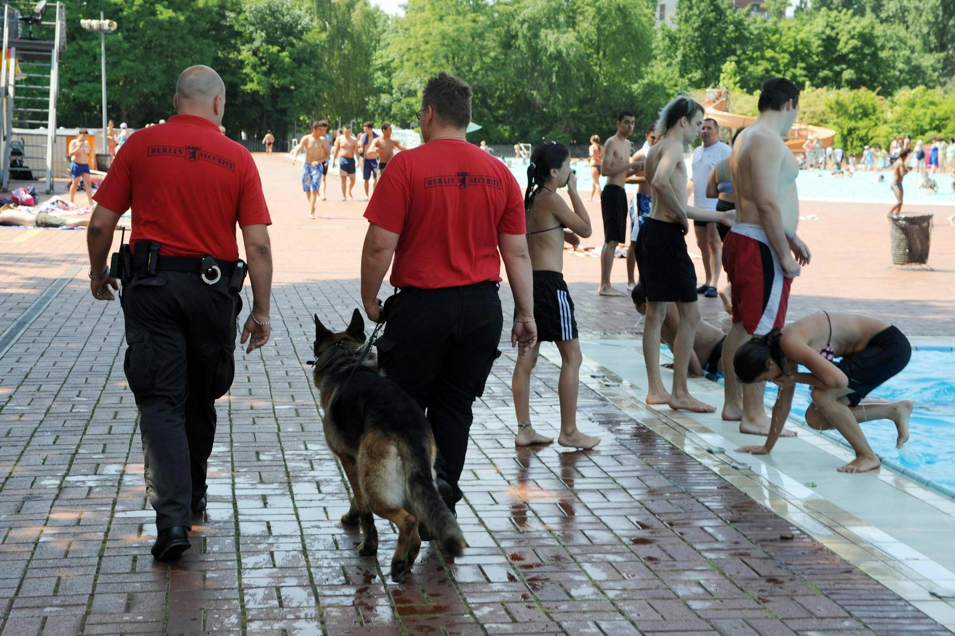 Mitarbeiter eines Sicherheitsdienstes patrouillieren mit Schäferhund am Beckenrand eines Berliner Freibads.