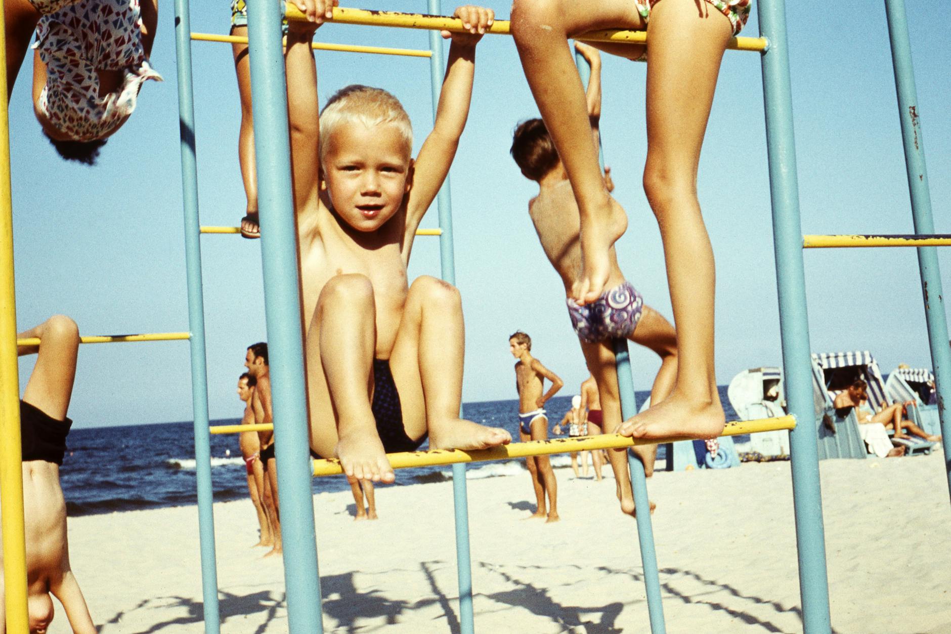 Sommer am Ostseestrand. Kinder spielen auf einem Klettergerüst am Strand. An Sonnencreme dachten damals die wenigsten.