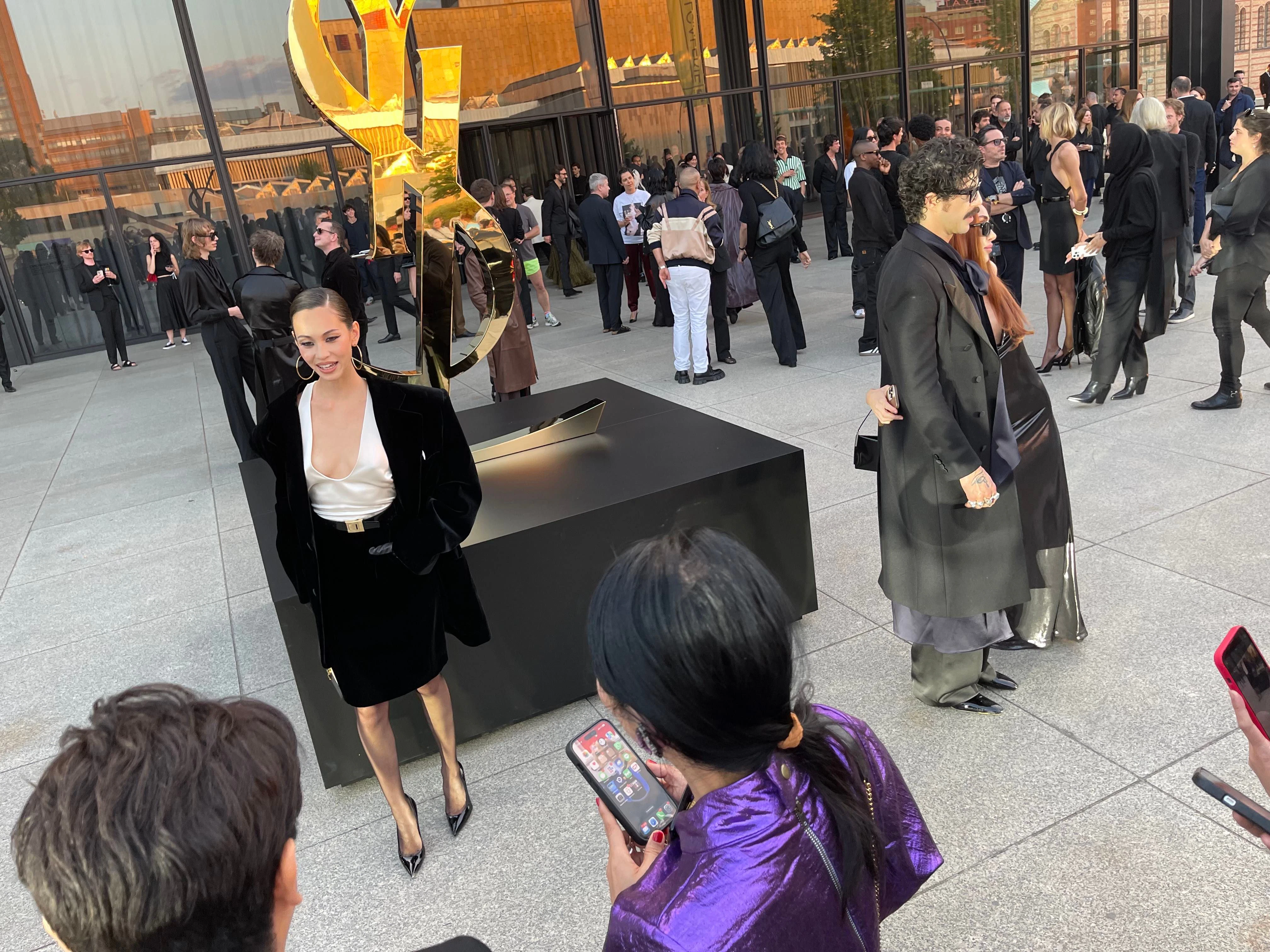 Auch diese Dame erscheint in einem aktuellen Look von Saint Laurent. Bezeichnend sind das tiefausgeschnittene Hemd und der breitschultrige Blazer.