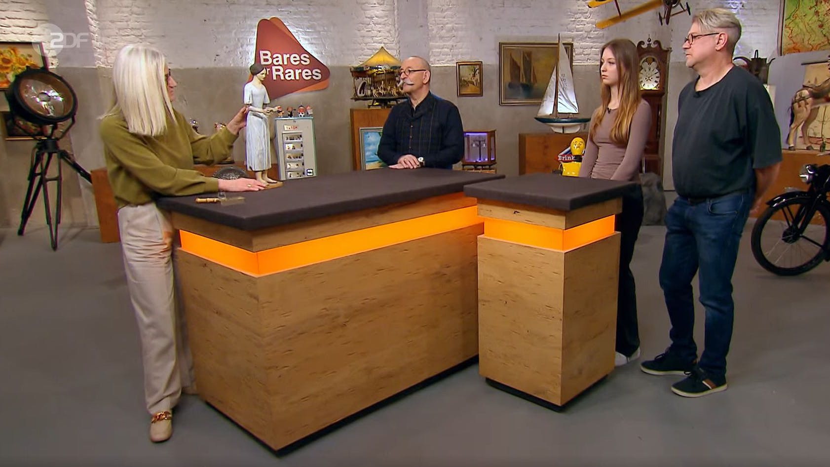 „Bares für Rares“-Expertin Dr. Friederike Werner (l.) erläutert den Besitzern und dem Moderator die Funktion der seltenen Puppe.