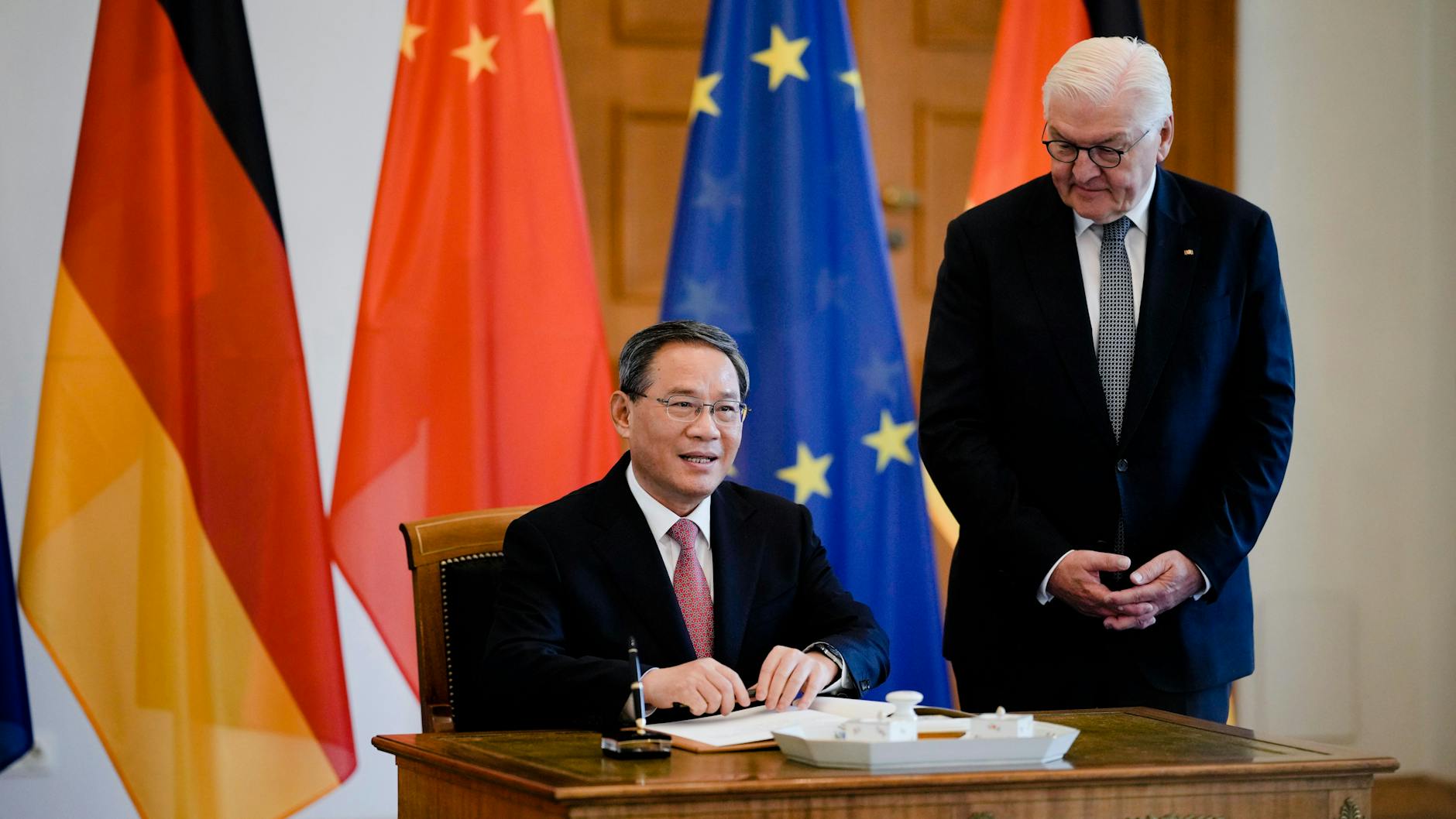 Chinas Ministerpräsident Li Quiang trägt sich ins Gästebuch ein, Bundespräsident Frank-Walter Steinmeier steht neben ihm.