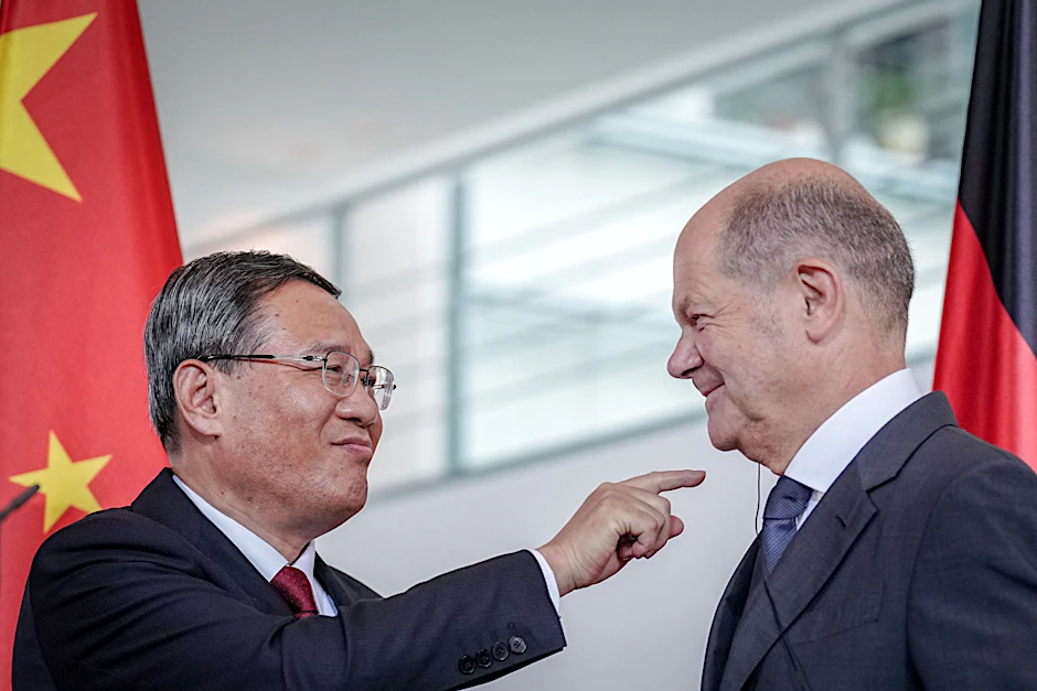 Li Qiang (l.) zeigt zum Ende des Pressestatements auf den Kopfhörer für die Übersetzung im Ohr von Bundeskanzler Olaf Scholz.&nbsp;