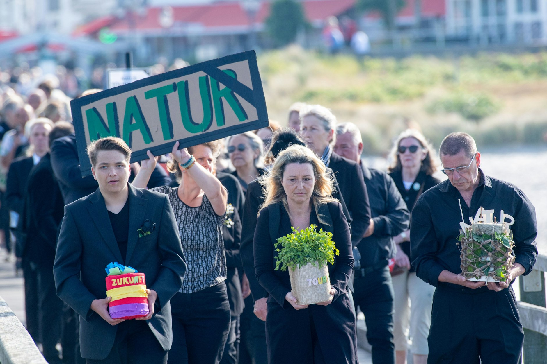 16.06.2023, Mecklenburg-Vorpommern, Binz: Teilnehmer bei dem Protest des Bündnisses „Rügens größter - Trauerzug“ halten Transparente. Der Streit um den Standort des geplantes Terminal für Flüssigerdgas (LNG) im Hafen Mukran hatten die Initiatoren einen Trauerzug organisiert.