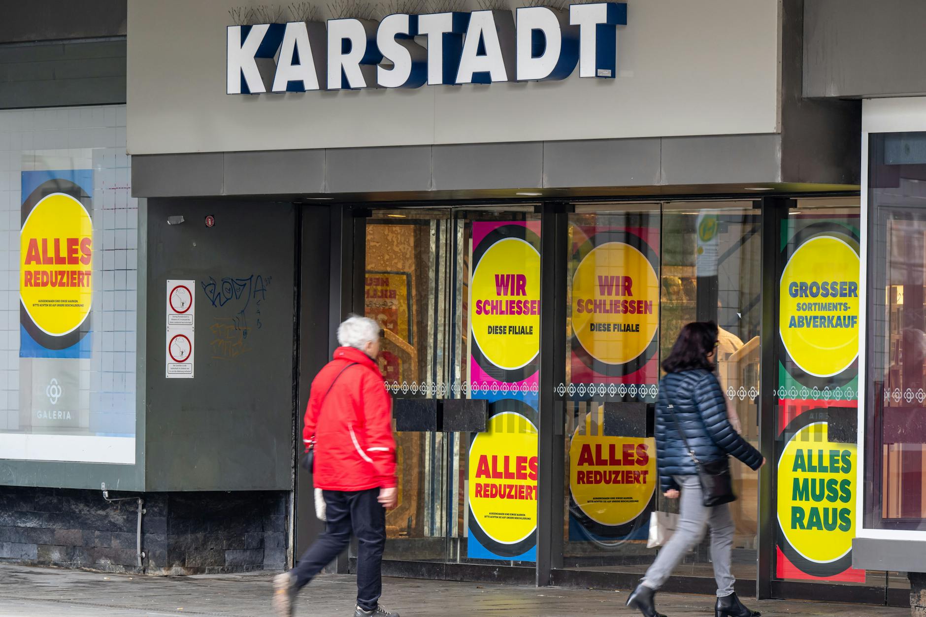 Schilder mit der Aufschrift „Wir schließen“ und „Alles muss raus“ kleben im Eingangsbereich einer Karstadt-Filiale in München.
