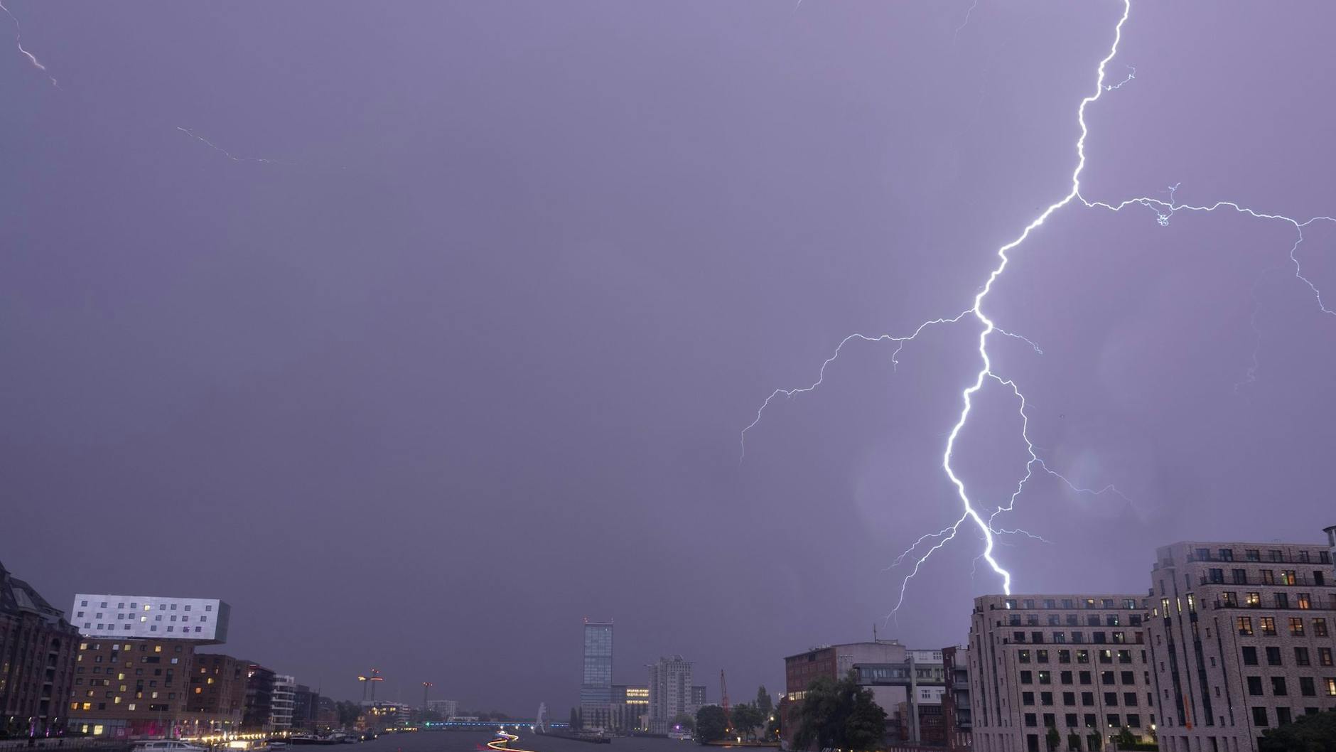 Ein Blitz entlädt sich am späten Abend über der Spree in Richtung Elsenbrücke am Himmel. 