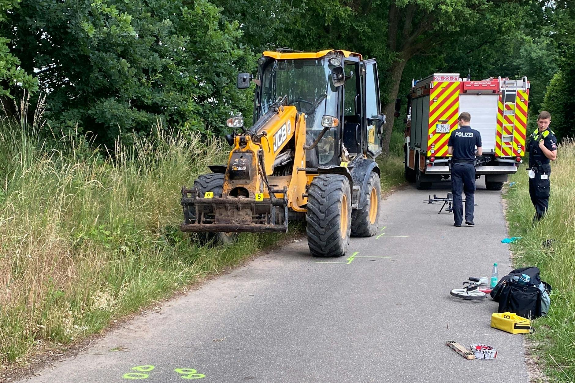 Polizeibeamte stehen neben dem Bagger nach dem Unfall auf einem Feldweg.