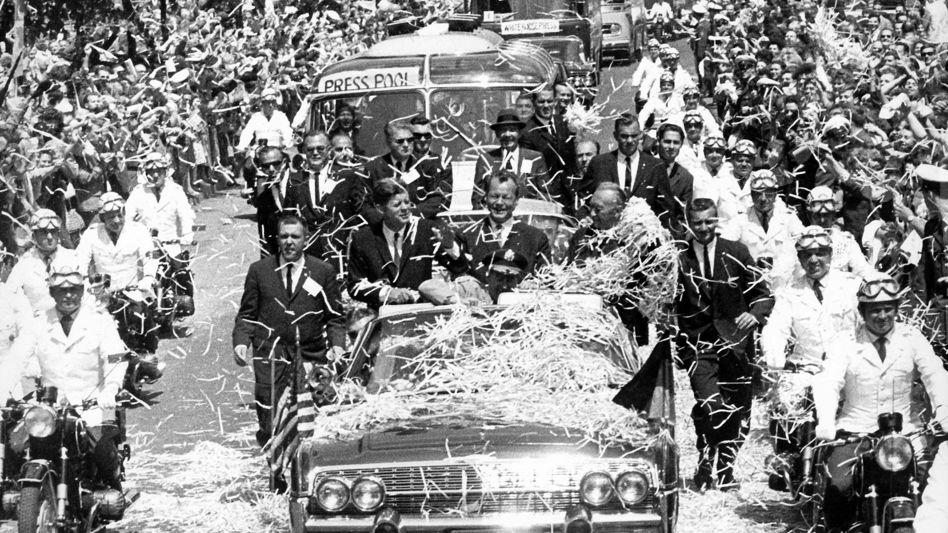 Triumphfahrt durch Berlin im Konfettiregen. Begleitet von einer Motorrad-Eskorte fahren der US-amerikanische Präsident John F. Kennedy, der damalige Regierende Bürgermeister von Berlin Willy Brandt (M.) und der damalige Bundeskanzler Konrad Adenauer in einem offenen Wagen am 26. Juni 1963 durch die Stadt.