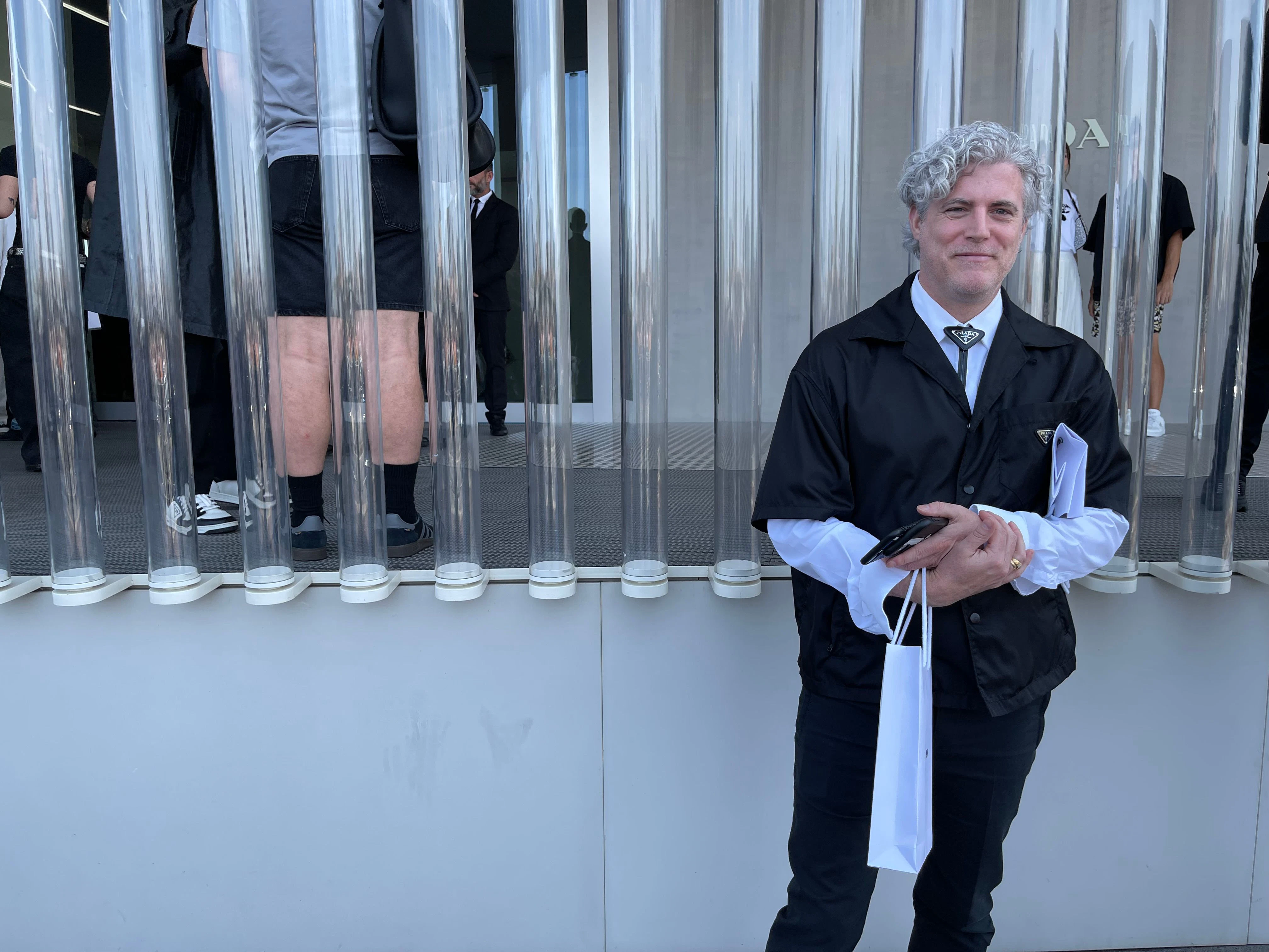 Ein fesch gekleideter Prada-Mitarbeiter mit schönen Locken wartet auf seine Gäste.&nbsp;