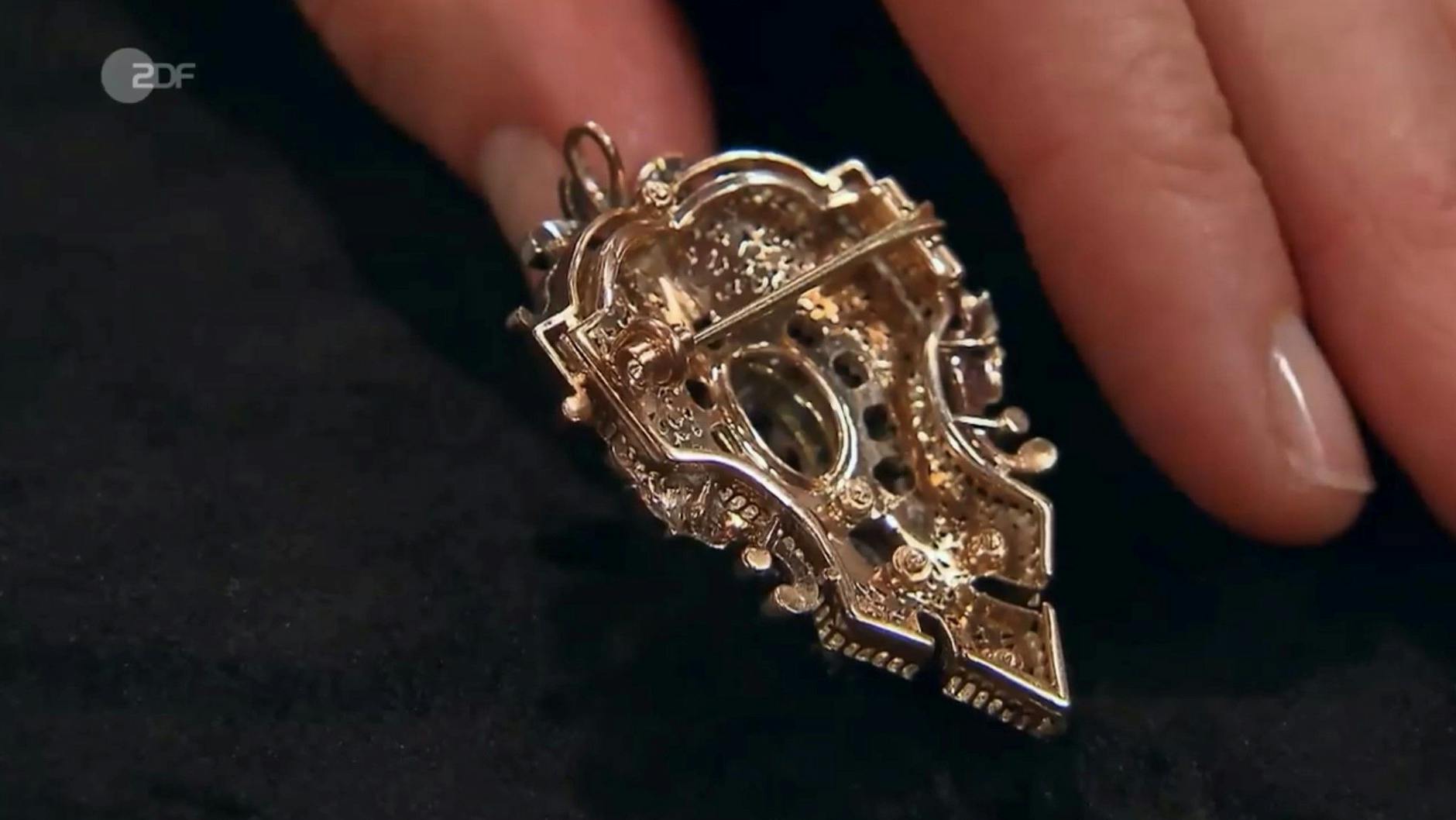 Die „Bares für Rares“-Expertin zeigt auf der Rückseite die Broschierung und die kleine Öse oben.