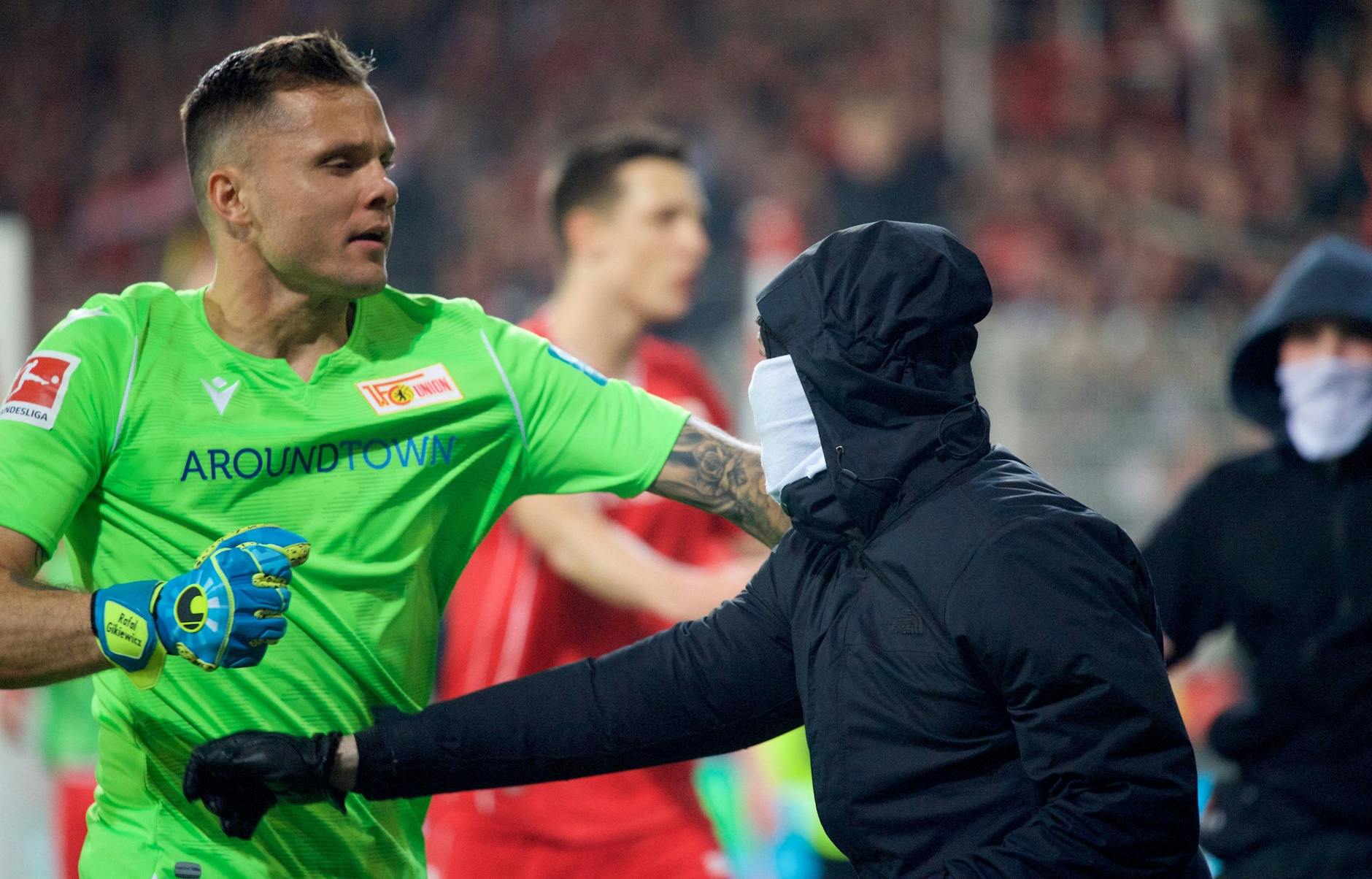 Union-Keeper Rafal Gikiewicz hält vermummte Fans von einem Platzsturm zurück.