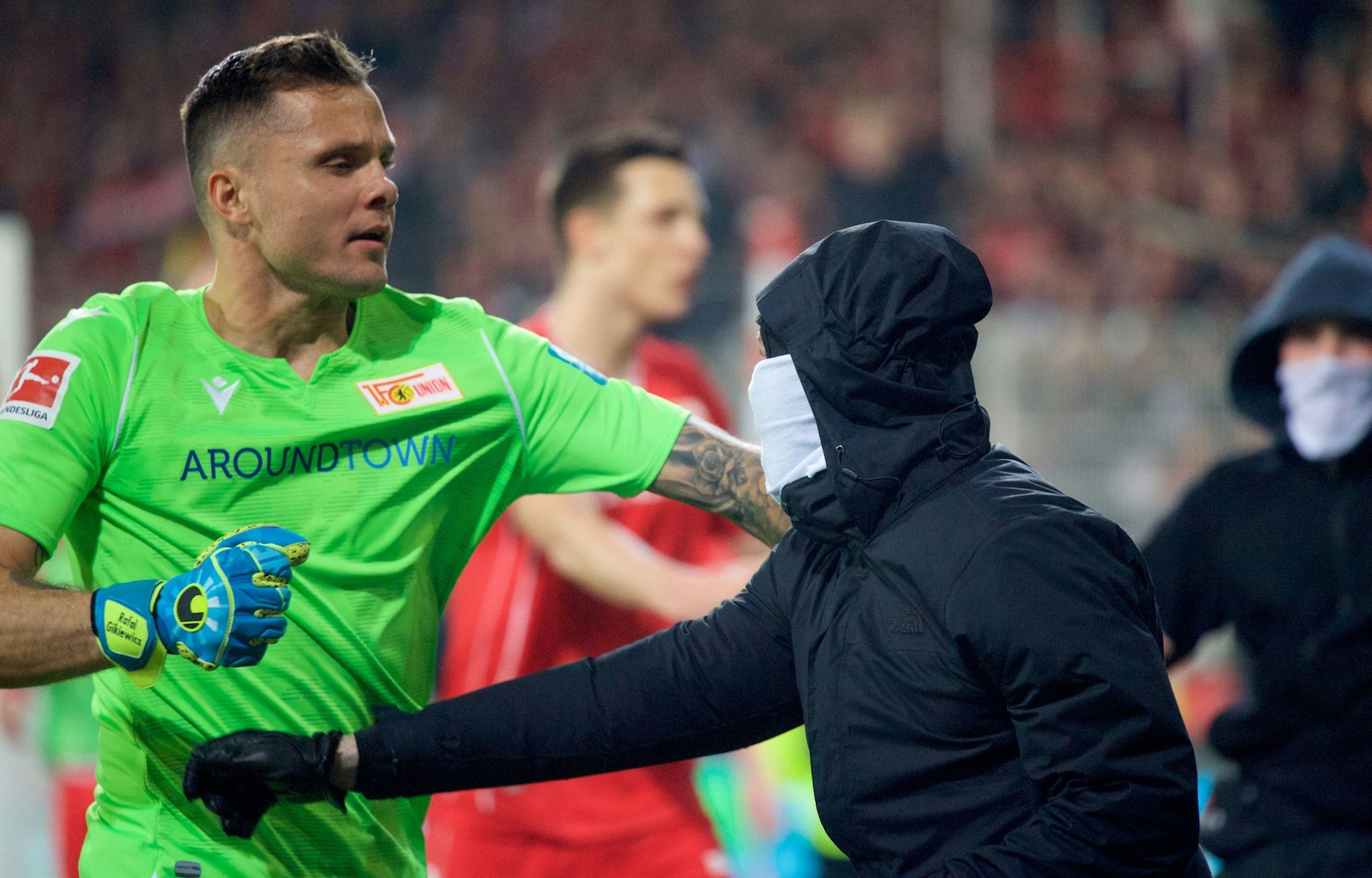 Union-Keeper Rafal Gikiewicz hält vermummte Fans von einem Platzsturm zurück.