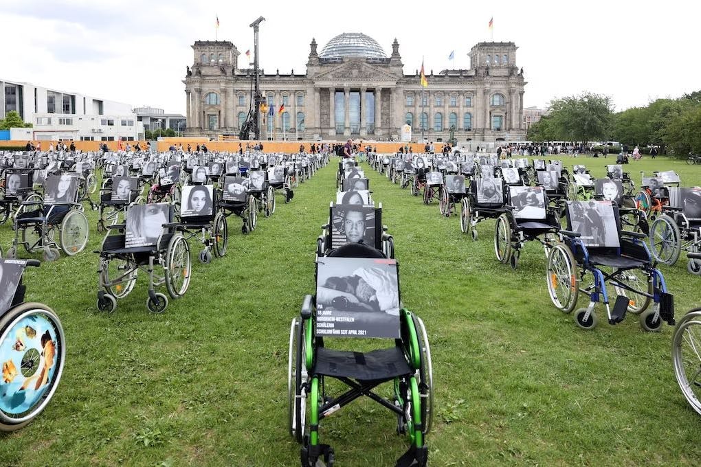 Hunderte Rollstühle vor dem Reichstagsgebäude mit Porträts von Menschen, die an den Spätfolgen von Corona leiden.