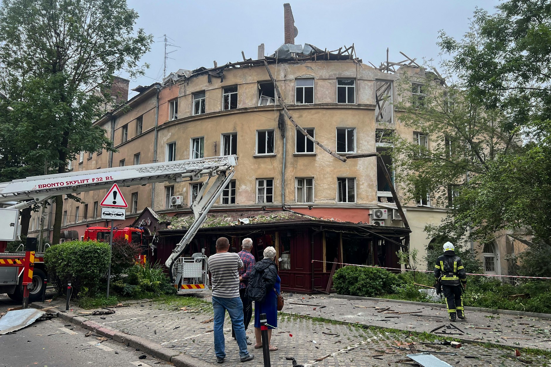 Lwiw: Menschen beobachten einen Feuerwehreinsatz nach einem Raketenangriff, bei dem ein Gebäude beschädigt wurde.