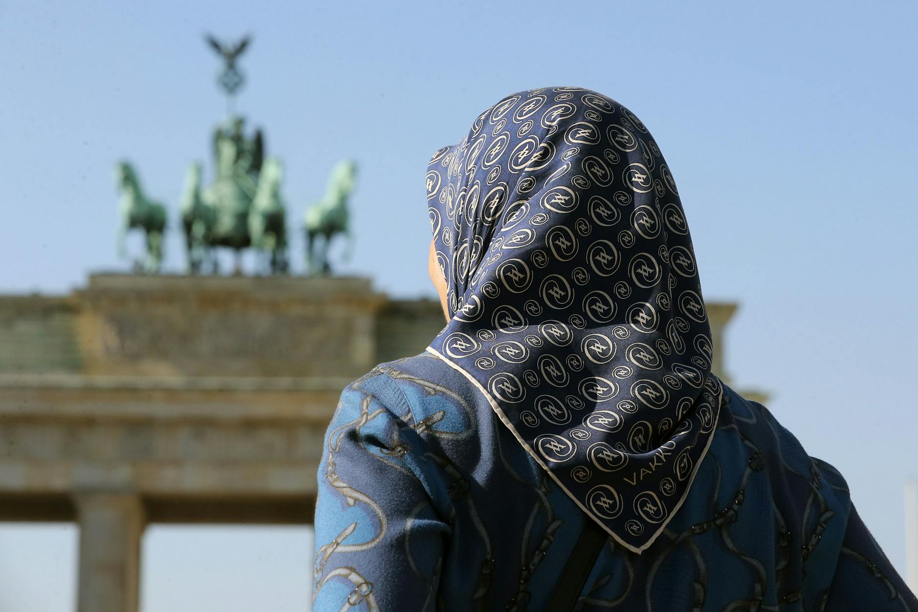 Eine muslimische Frau mit Kopftuch steht vor dem Brandenburger Tor.