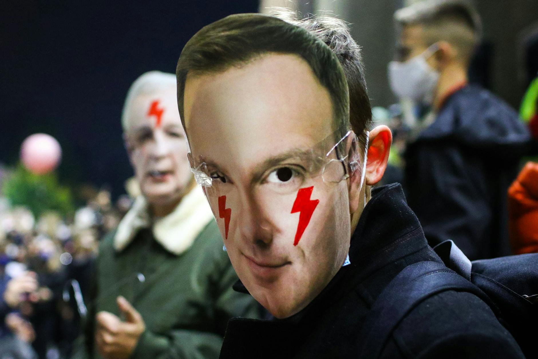 28. Oktober 2020, Krakau: Ein Demonstrant trägt eine Maske mit dem Gesicht des polnischen Präsidenten Andrzej Duda und rote Blitze als Symbol des Frauenstreiks auf seinen Wangen.