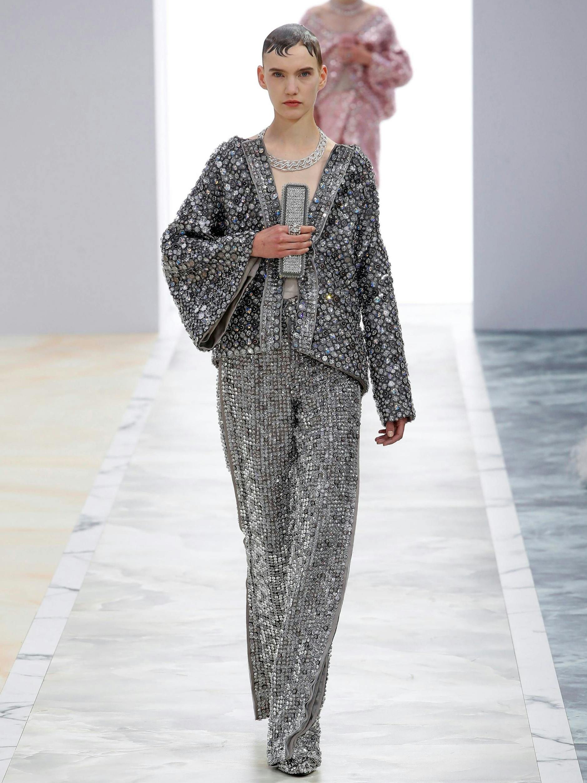 In der hypereleganten Fendi-Couture von Kim Jones sind es die Details, die beeindrucken. Damit sind nicht nur die unzähligen funkelnden Steine gemeint, mit denen der glamouröse Zweiteiler übersäht ist, sondern auch die glitzernde Clutch, die an einem Fingerring sitzt. Prädikat: besonders wertvoll.