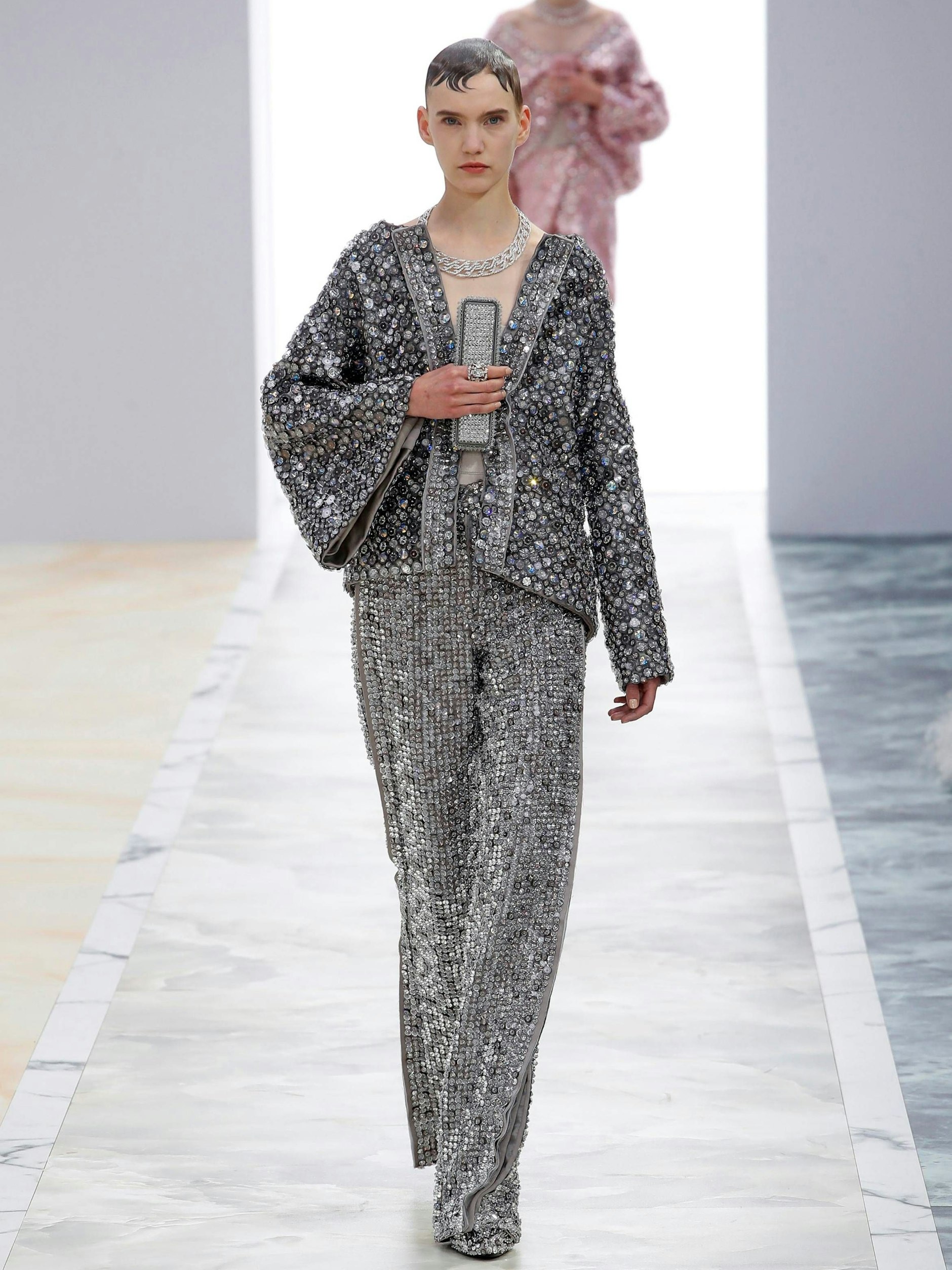 In der hypereleganten Fendi-Couture von Kim Jones sind es die Details, die beeindrucken. Damit sind nicht nur die unzähligen funkelnden Steine gemeint, mit denen der glamouröse Zweiteiler übersäht ist, sondern auch die glitzernde Clutch, die an einem Fingerring sitzt. Prädikat: besonders wertvoll.