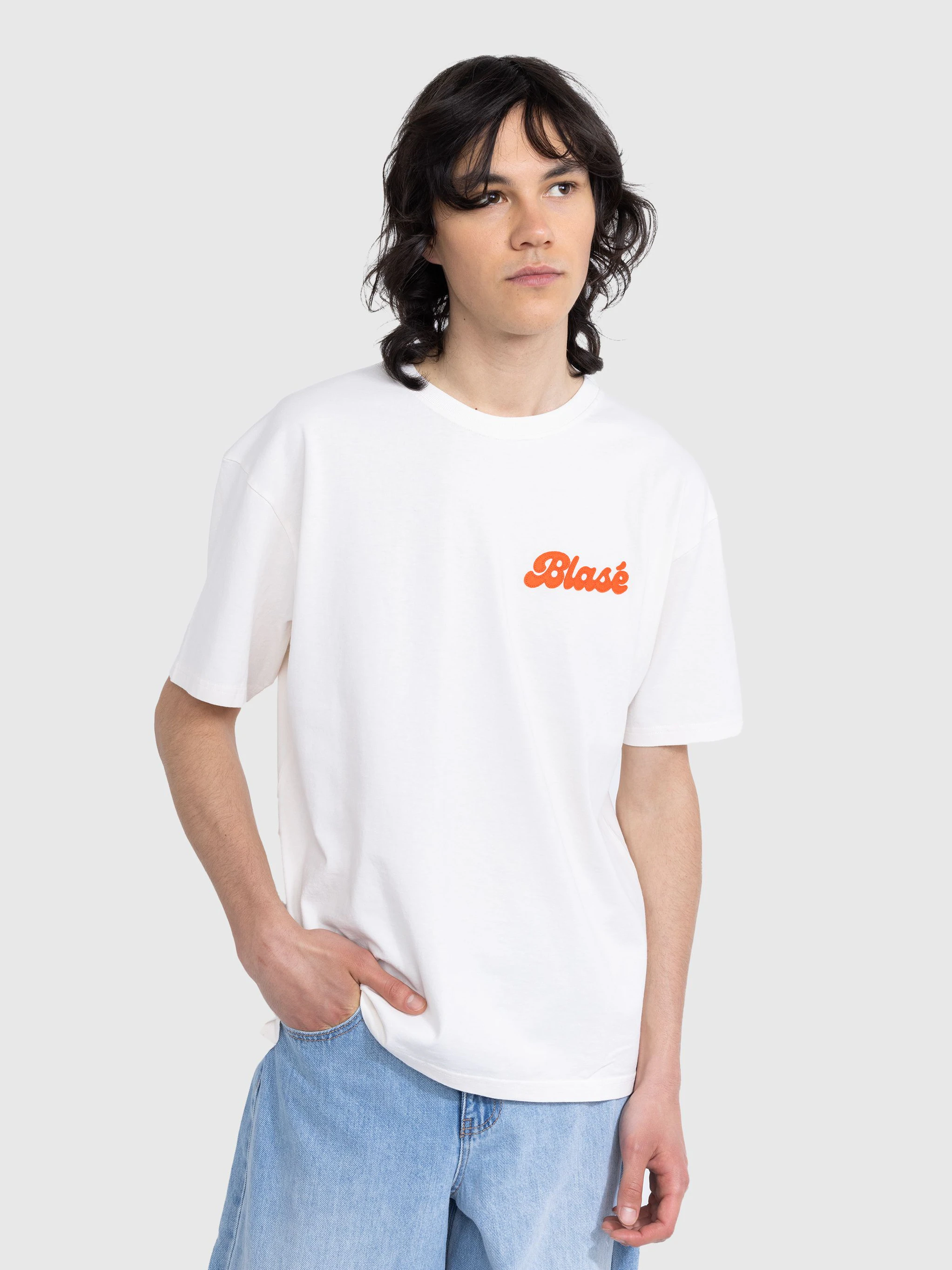 Was wäre die Streetwear ohne ihre Logos und Patches. Gerade das weiße T-Shirt bietet ja die perfekte Fläche dafür. Von Highsnobiety aus Berlin gibt es daher eine ganze Menge weißer T-Shirts, aber nicht ohne Messages. Aus der Serie „Not In Paris“, die während der Pandemie gelauncht wurde und sich auf die damals ausbleibende Reiserei zur Paris Fashion Week bezog, stammt dieses Unisex-Shirt. Das aufgenähte „Blasé“-Patch in Orange passt bestens zum Hellblau einer Sommerjeans.