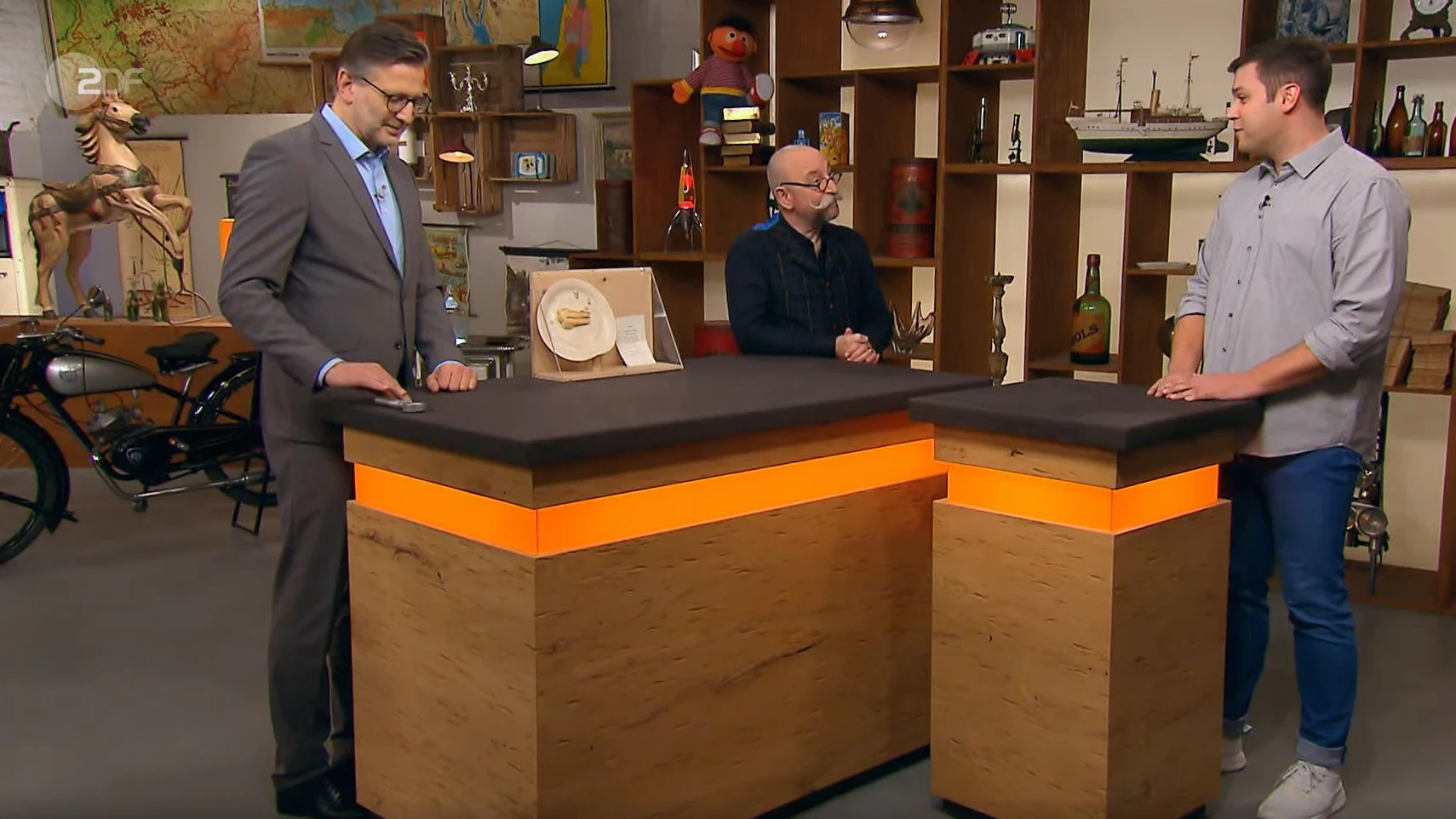 Verkäufer Dominik (r.) kommt mit einer abenteuerlichen Geschichte um die Ecke, Moderator Horst Lichter ist skeptisch, aber „Bares für Rares“-Experte Detlev Kümmel (l.) kann aufklären.