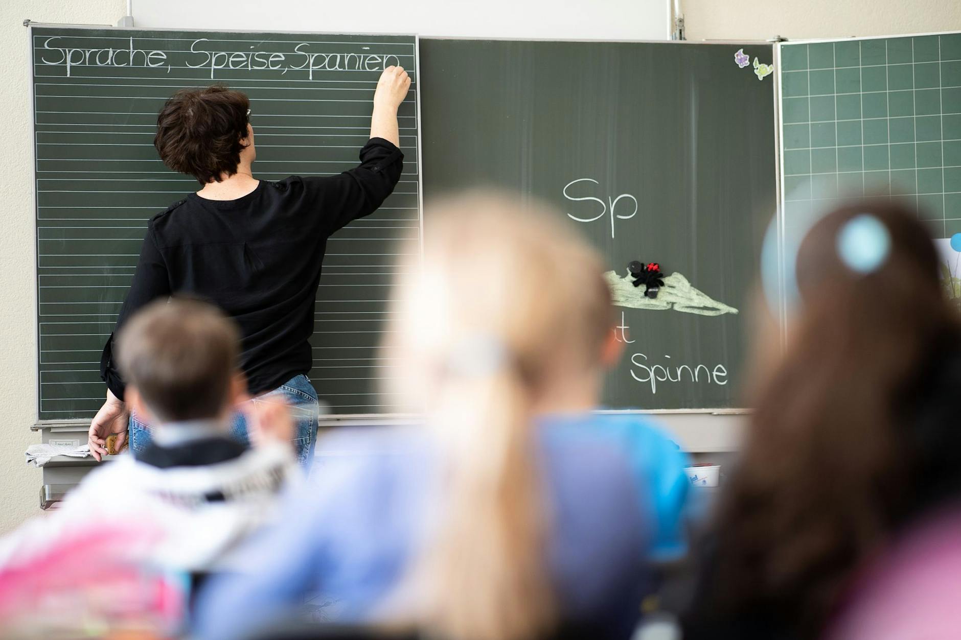 Eine Lehrerin schreibt in einer Grundschule Wörter mit „Sp“ am Anfang an eine Tafel.