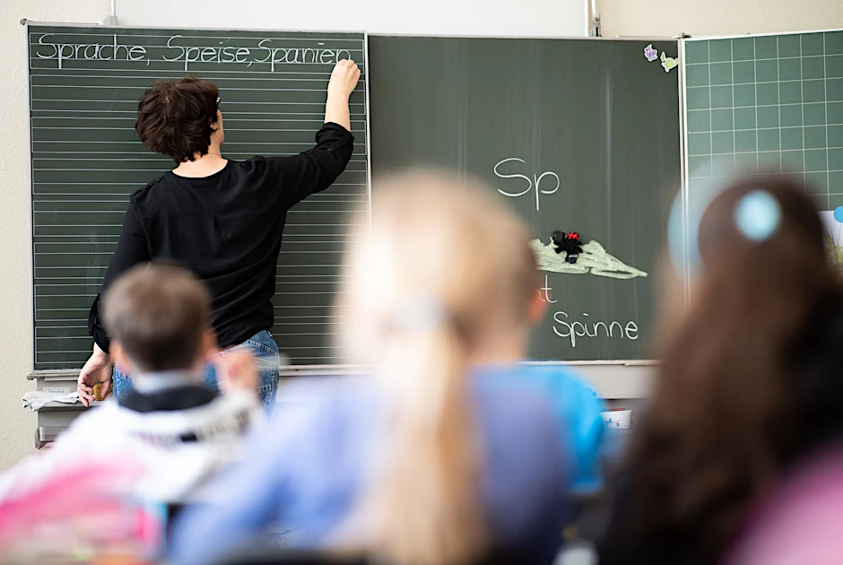 Eine Lehrerin schreibt in einer Grundschule Wörter mit „Sp“ am Anfang an eine Tafel.