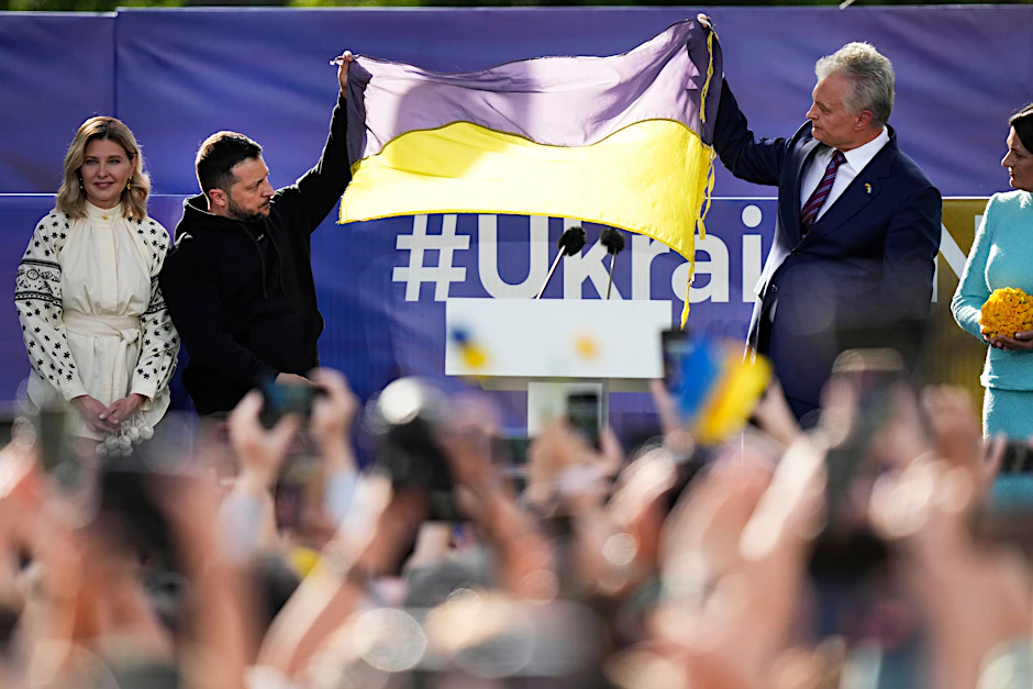 Der ukrainische Präsident Wolodymyr Selenskyj (2.v.l), seine Frau Olena Selenska (l.) und Gitanas Nauseda (r.), Präsident von Litauen, halten eine ukrainische Fahne hoch, während sie sich am Rande des Nato-Gipfels an die Menge wenden.