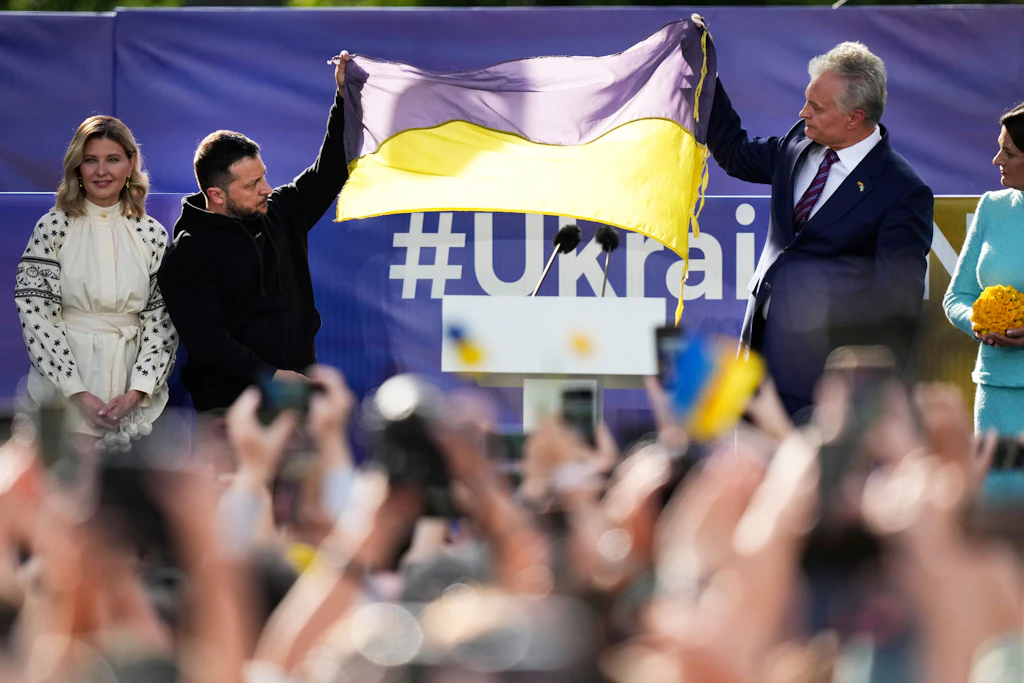Der ukrainische Präsident Wolodymyr Selenskyj (2.v.l), seine Frau Olena Selenska (l.) und Gitanas Nauseda (r.), Präsident von Litauen, halten eine ukrainische Fahne hoch, während sie sich am Rande des Nato-Gipfels an die Menge wenden.