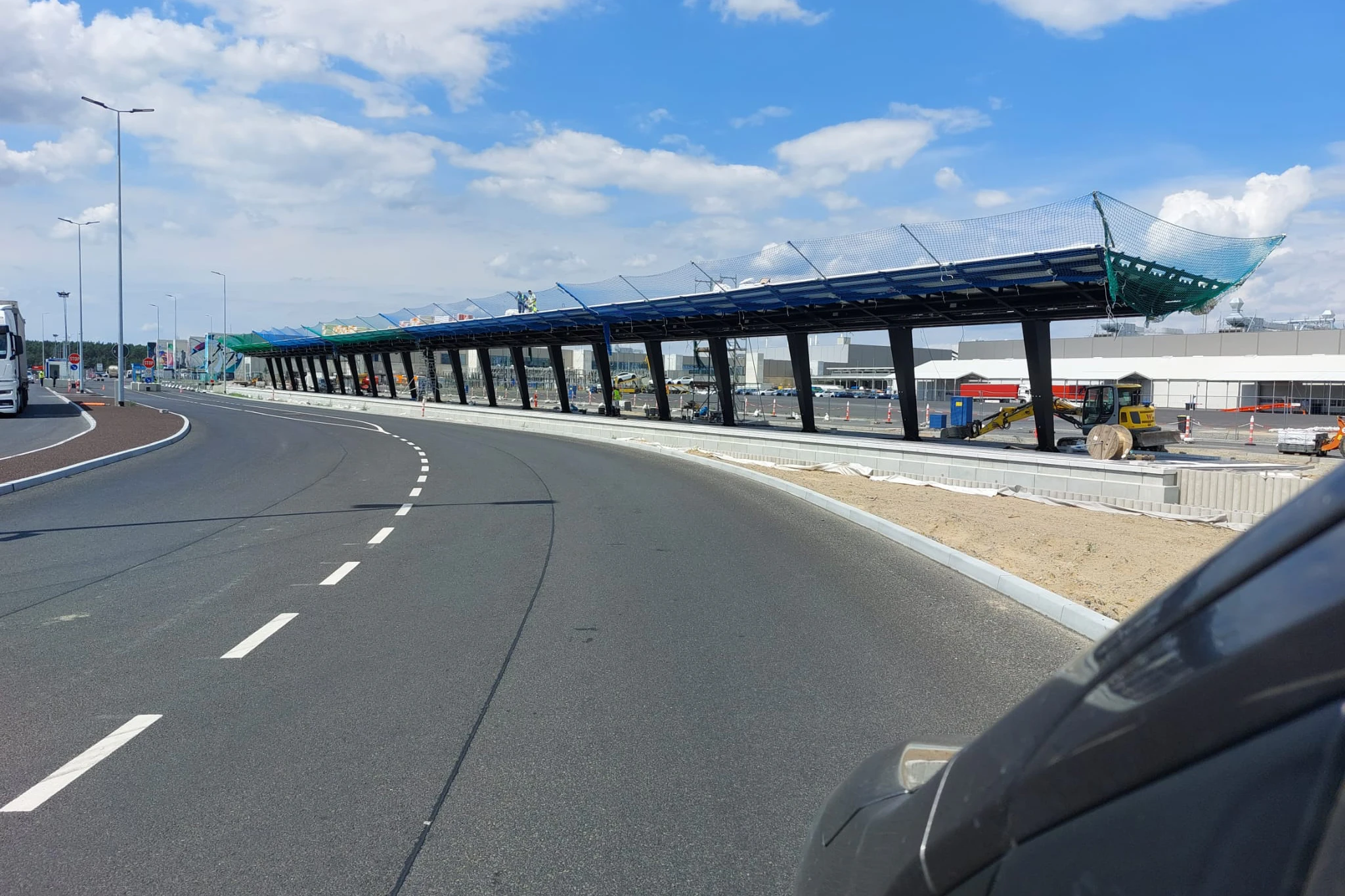 Das ist der neue Bahnhof Tesla Süd. Als das Foto im Juli aufgenommen wird, stehen schon die Dachstützen, und das Dach ist montiert. Nebenan werden Gleise verlegt. Hier sollen die Züge nach Erkner beginnen.