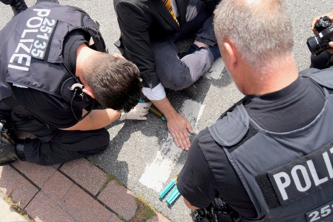 Ein Klimaaktivist hat sich mit der Handfläche auf dem Asphalt einer Straße in der Bremer Innenstadt festgeklebt. Polizisten lösen die Hand vom Asphalt.