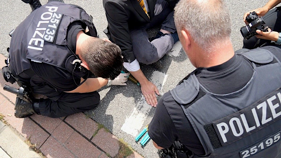 Ein Klimaaktivist hat sich mit der Handfläche auf dem Asphalt einer Straße in der Bremer Innenstadt festgeklebt. Polizisten lösen die Hand vom Asphalt.