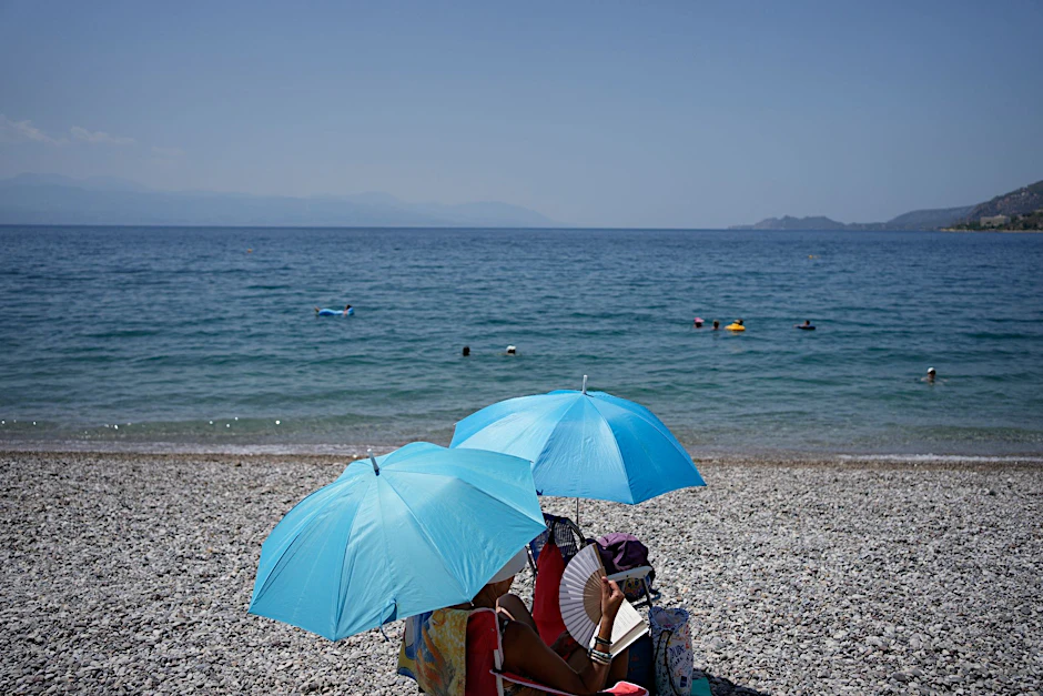 Da helfen nur noch Sonnenschrirme und ein Handventilator: Eine Frau am Strand von Loutraki.  