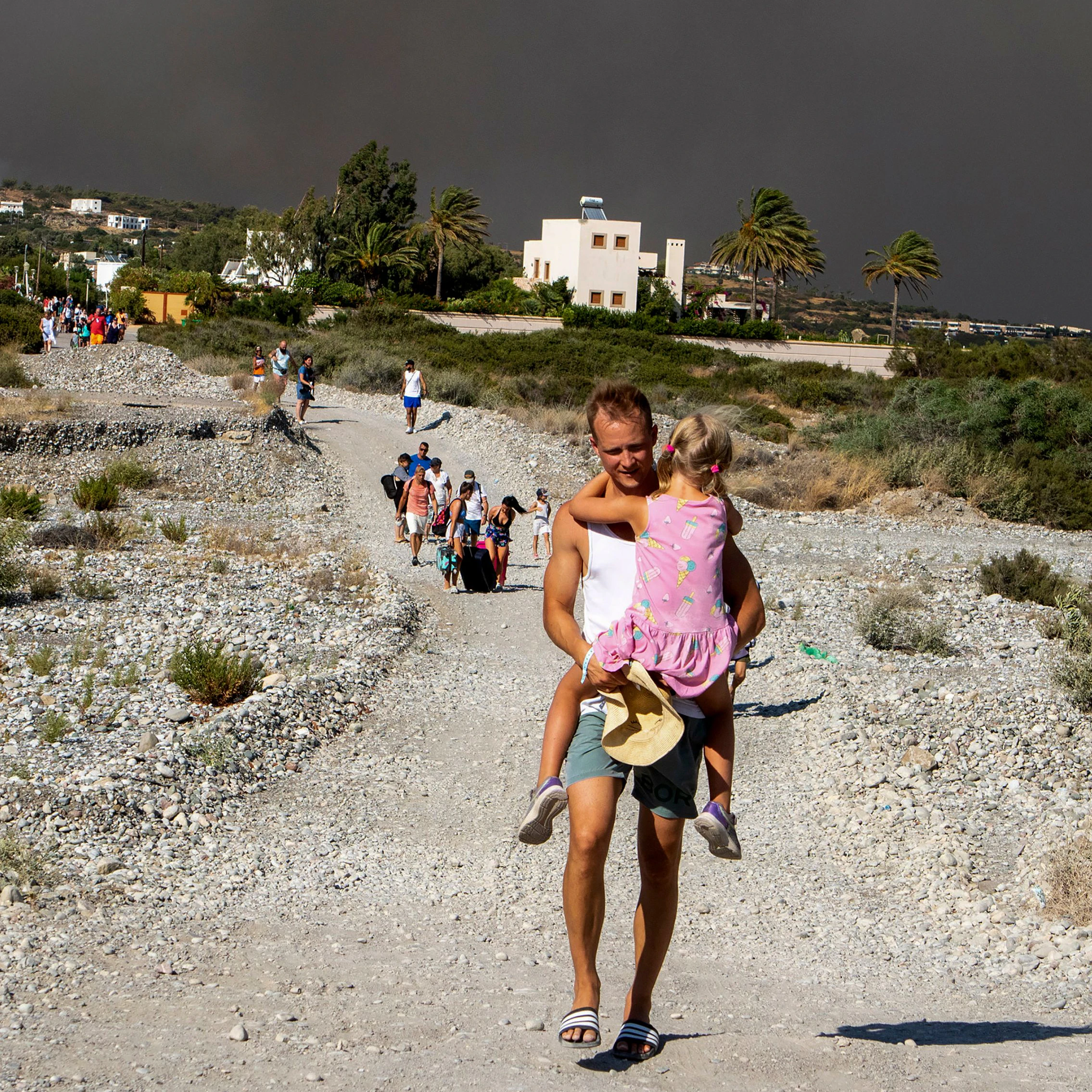 Ein Mann trägt ein Kind, als sie ein Gebiet verlassen, in dem ein Waldbrand auf der griechischen Insel Rhodos wütet. 