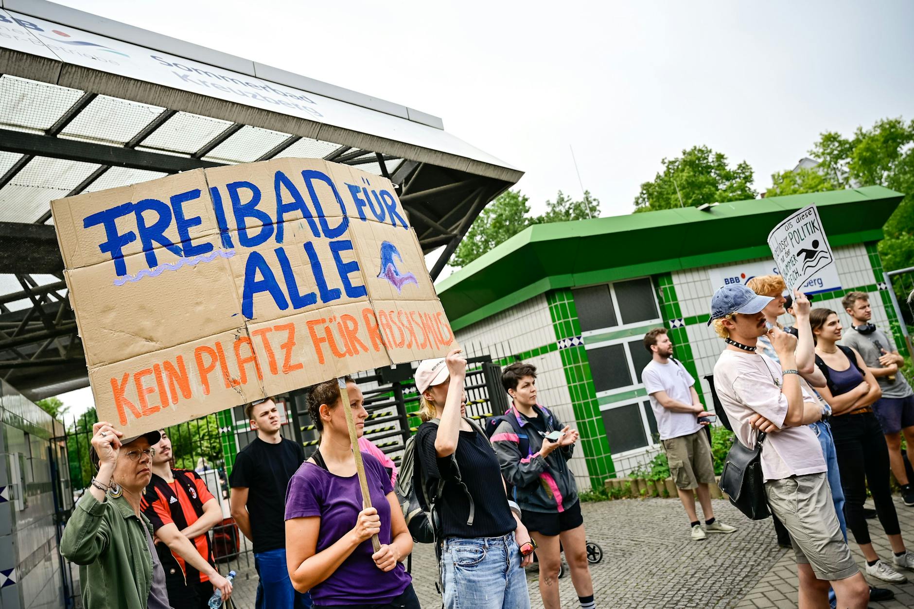 Die Menschen auf der Kundgebung vor dem Prinzenbad fordern, dass Geld in Soziales, Schwimmbadpersonal und Sanierungen von Bädern fließt – statt in mobile Polizeiwachen.