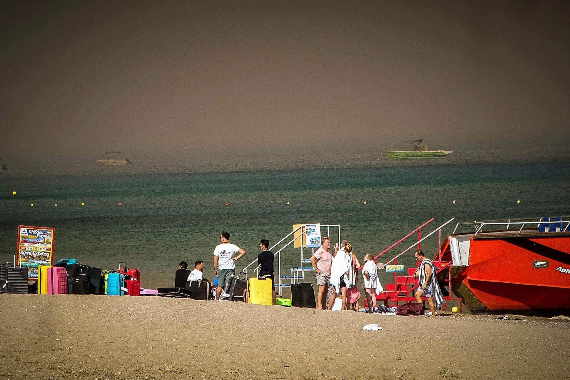 Touristen stehen an einem Strand, wohin sie wegen eines Waldbrandes auf der griechischen Insel Rhodos in Sicherheit gebracht worden sind. 