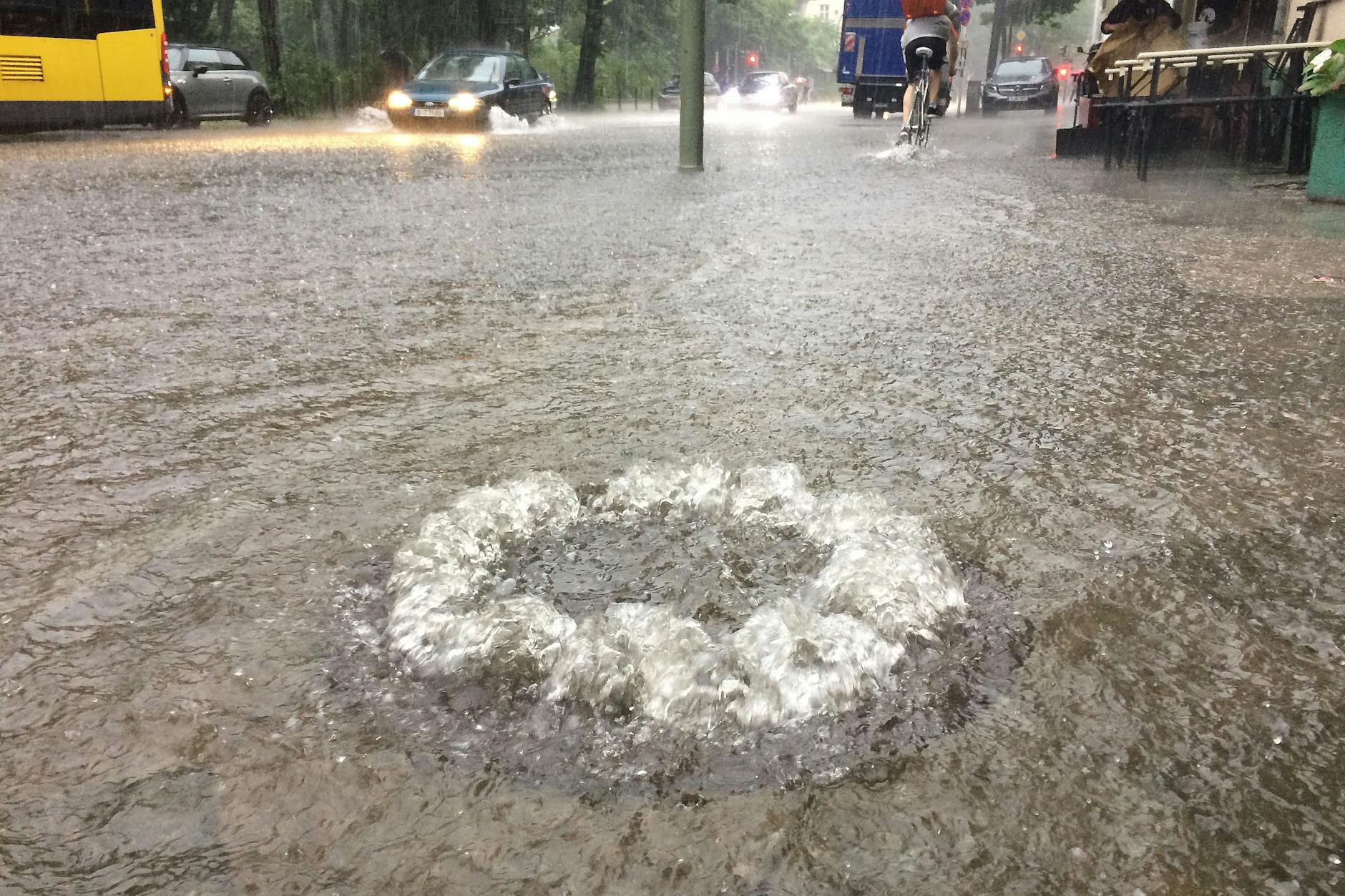So sah es hier auch schon mal aus: Wasser sprudelt am 29. Juni 2017 in Berlin auf einer überfluteten Straße im Stadtteil Schöneberg aus einem Gully. 