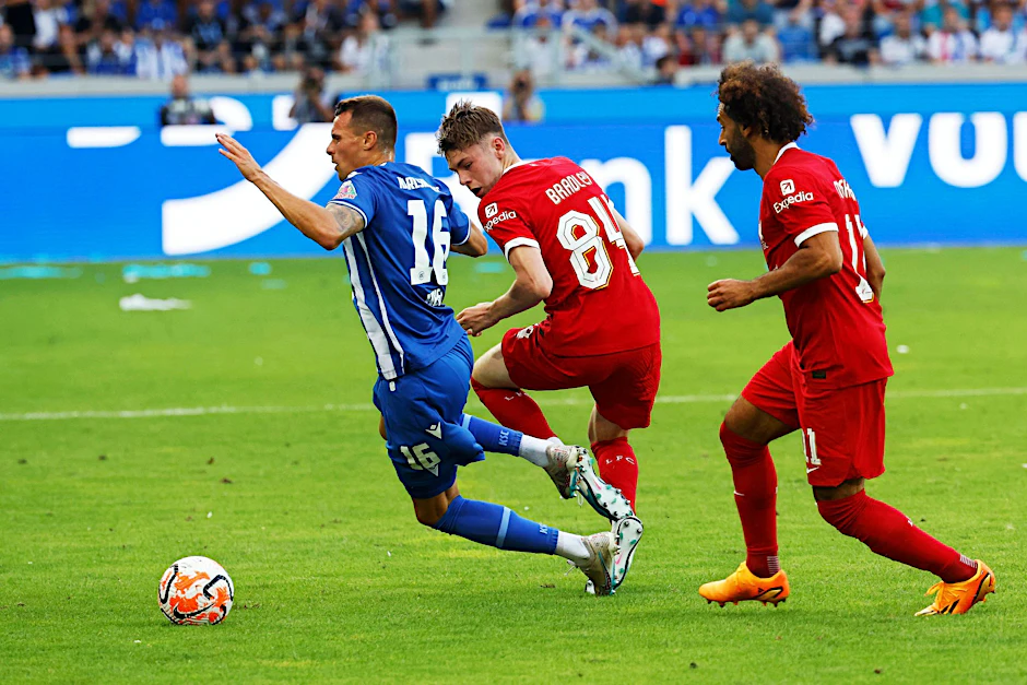 Karlsruhes Philip Heise (l-r) in Aktion gegen Liverpools Conor Bradley und Mohamed Salah.  