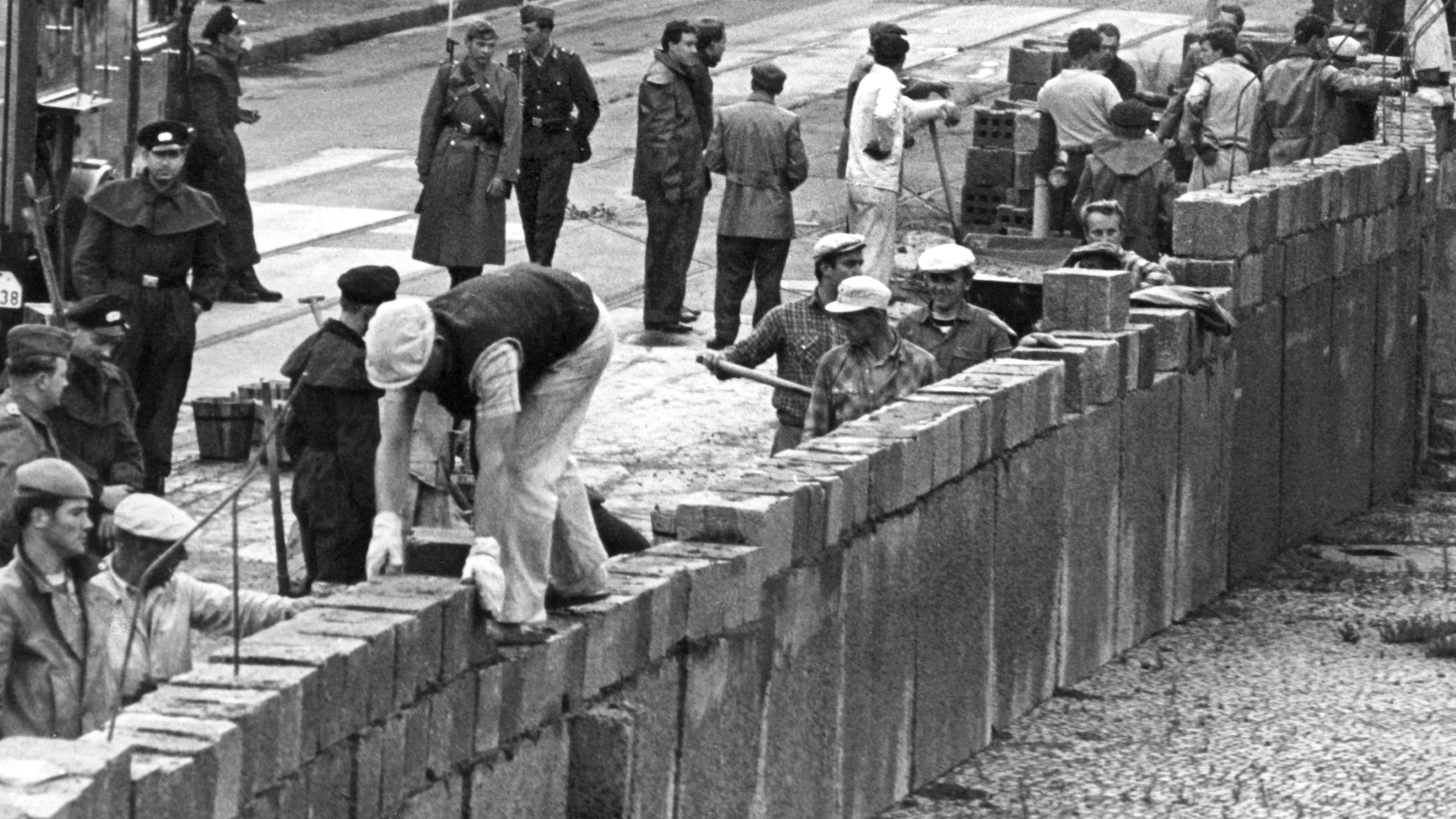 Das Archivbild vom 18.8.1961 zeigt eine Ost-Berliner Maurerkolonne, die unter Aufsicht von bewaffneten DDR-Volkspolizisten am 18.8.1961 an der sowjetisch-amerikanischen Sektorengrenze am Potsdamer Platz eine mannshohe Mauer errichtet. Am Morgen des 13. August hatten DDR-Streitkräfte unter dem Decknamen „Aktion Rose“ damit begonnen, den Ostteil der Stadt mit Straßensperren in Richtung Westen zu sperren.&nbsp;
