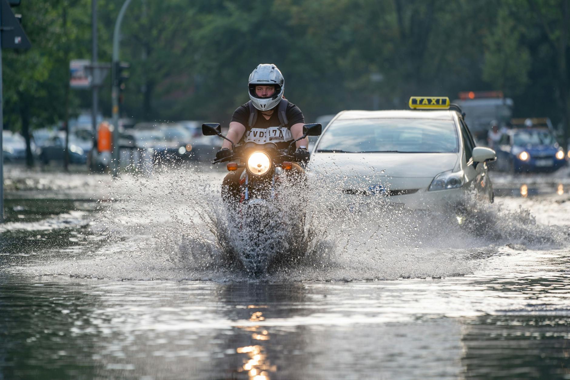 Ein Motorradfahrer fährt vor einem Taxi auf der überfluteten Tiergartenstraße. Auch in Berlin gibt es inzwischen immer wieder Starkregen.