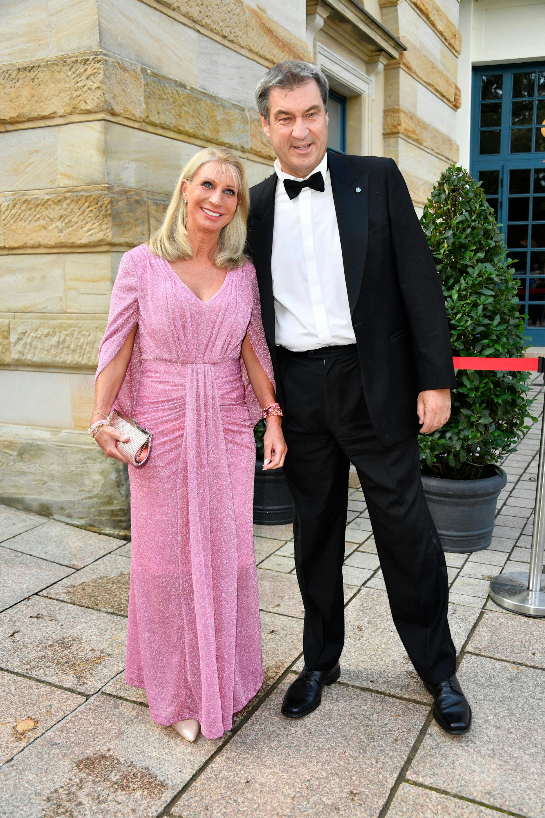 <strong>FLOP:</strong> Das Ehepaar Söder hatte an diesem Abend keinen guten Lauf: Sein Hemd hätte eine Nummer kleiner, ihr Kleid eine Nuance weniger verspielt sein dürfen. Auch der Smoking des Bayerischen Ministerpräsidenten hat nicht nur gute Momente: Das aufsteigende Revers etwa ist viel zu groß und viel zu spitz – als wollte <strong>Markus Söder</strong> seine Konzert-Sitznachbarn mit den zickig ausgestellten Kragenspitzen aufspießen. Ins Berliner Freibad wäre er mit solch waffenscheinpflichtiger Textilie jedenfalls nicht hereingekommen. Das Abendkleid von Gattin <strong>Karin Baumüller-Söder</strong> wiederum hätte schon mehr Ecken und Kanten vertragen können: Seine Faltendetails und Drapierungen wirken zu spielerisch, das Rosa etwas arg mädchenhaft. Besser aufgehoben wäre sie damit auf der Premiere des „Barbie“-Films gewesen.