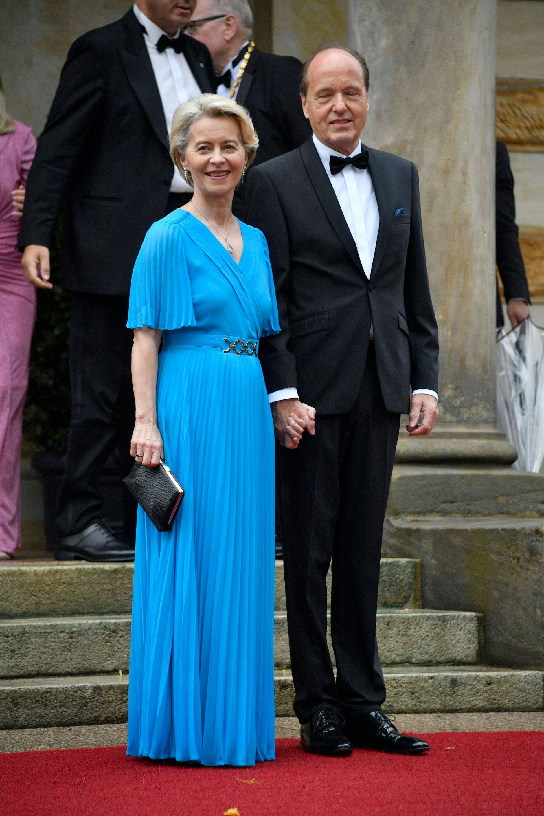 <strong>FLOP:</strong> Eine ungünstige Wahl hat <strong>Ursula von der Leyen</strong> getroffen: Mit seinen plissierten Flatterärmeln, dem plissierten Rock und dem wenig modernen Gürteldetail wirkt ihr Kleid furchtbar altbacken – wie ein Mottenkisten-Fund aus den 1950ern, der selbst im Humana am Frankfurter Tor keine Abnehmerin mehr gefunden hätte. Geradezu unverzeihlich ist die viel zu große, viel zu schwarze Abendtasche, die einfach nicht zur mittelblauen Farbe – übrigens auch ein absolut altmodischer Ton – ihres Kleides passen will. Immerhin: Der Rockteil endet den perfekten Zentimeter über dem Boden, eine hervorragende Länge – das hat die Präsidentin der Europäischen Kommission vielen Festspiel-Gästinnen voraus. Und: Ehemann&nbsp;<a href="https://www.google.com/search?rlz=1C1GCEA_enDE947DE947&amp;q=Heiko+von+der+Leyen&amp;stick=H4sIAAAAAAAAAONgVuLSz9U3SDYxTK8sfMRoyi3w8sc9YSmdSWtOXmNU4-IKzsgvd80rySypFJLgYoOy-KR4uJC08SxiFfZIzczOVyjLz1NISS1S8EmtTM0DAJHD1sBcAAAA&amp;sa=X&amp;ved=2ahUKEwi4tK2l1a6AAxXFSPEDHV6EB-wQzIcDKAB6BAgTEAE"><strong>Heiko von der Leyen</strong></a>&nbsp;kann im wirklich gut geschnittenen Anzug glänzen.