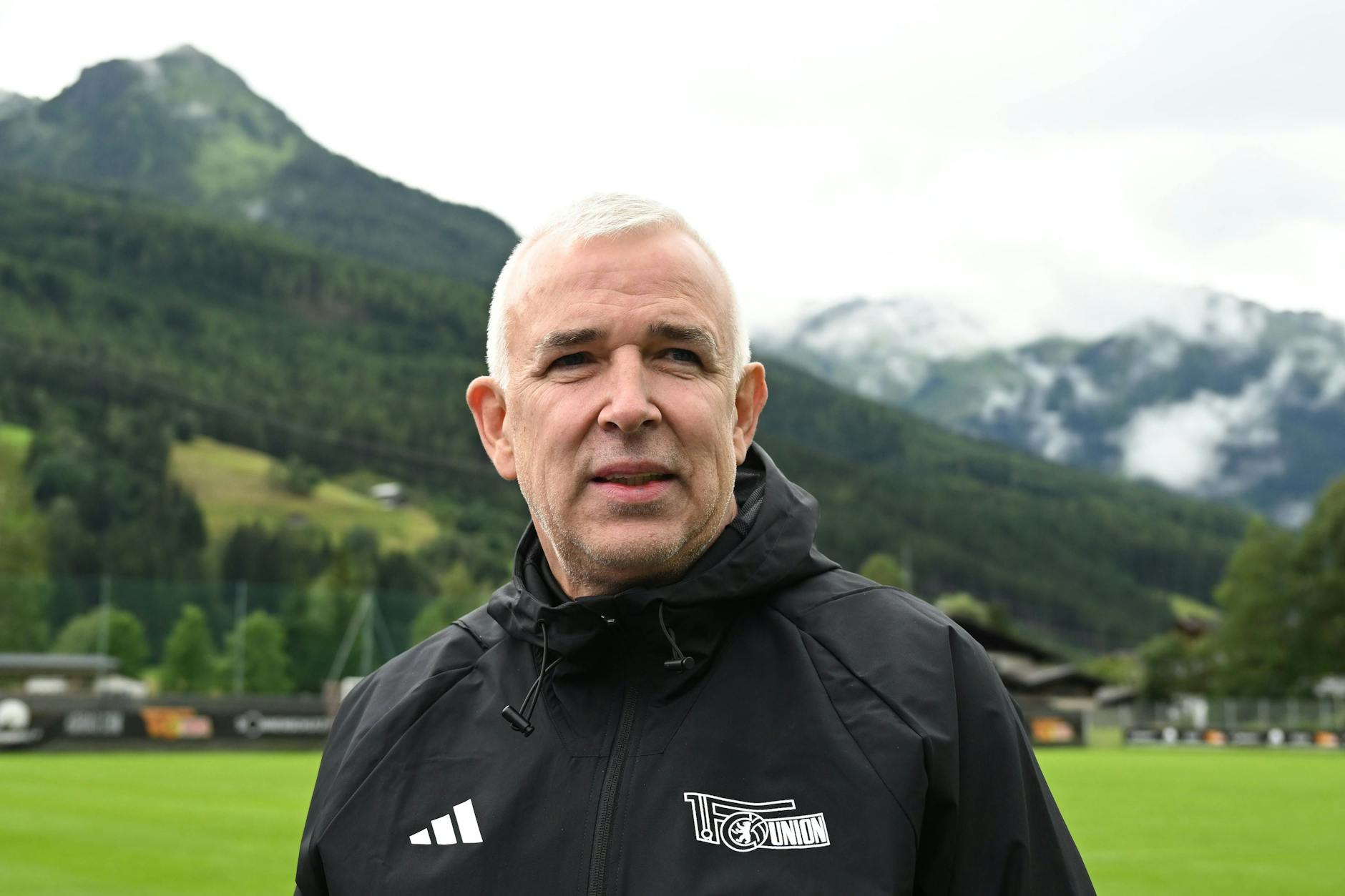 Unions Präsident Dirk Zingler steht im Trainingslager vor der Bergkulisse und macht sich so seine Gedanken über das liebe Geld.