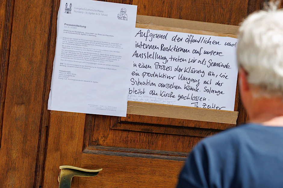 An der Eingangstür zur Nürnberger Kirche St. Egidien hängen eine Pressemitteilung so wie ein handgeschriebener Zettel zur vorübergehenden Schließung der Ausstellung „Jesus liebt“.