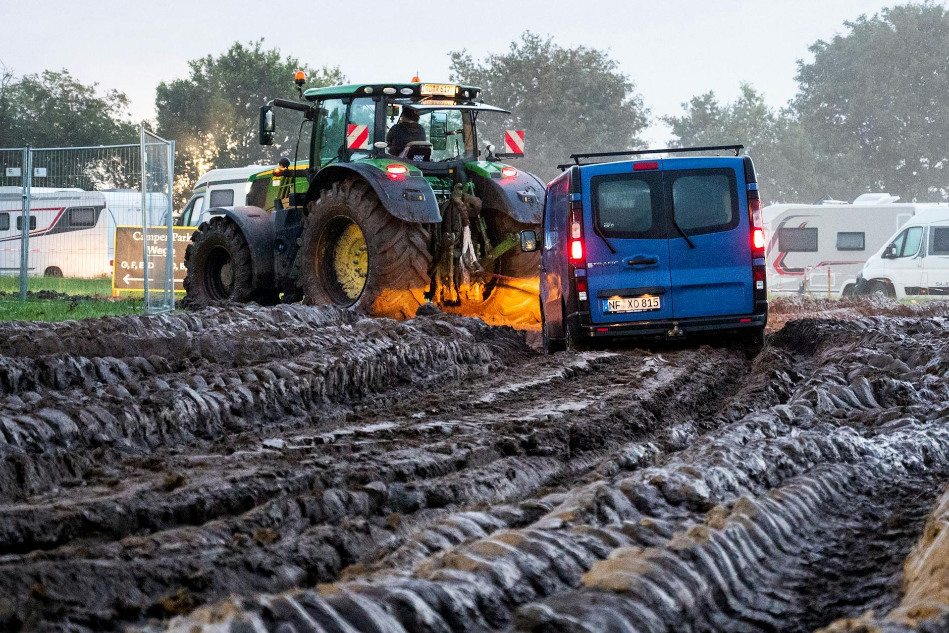 Autos werden mithilfe eines Traktors auf das Gelände des Heavy-Metal-Festivals in Wacken durch den Schlamm gezogen.