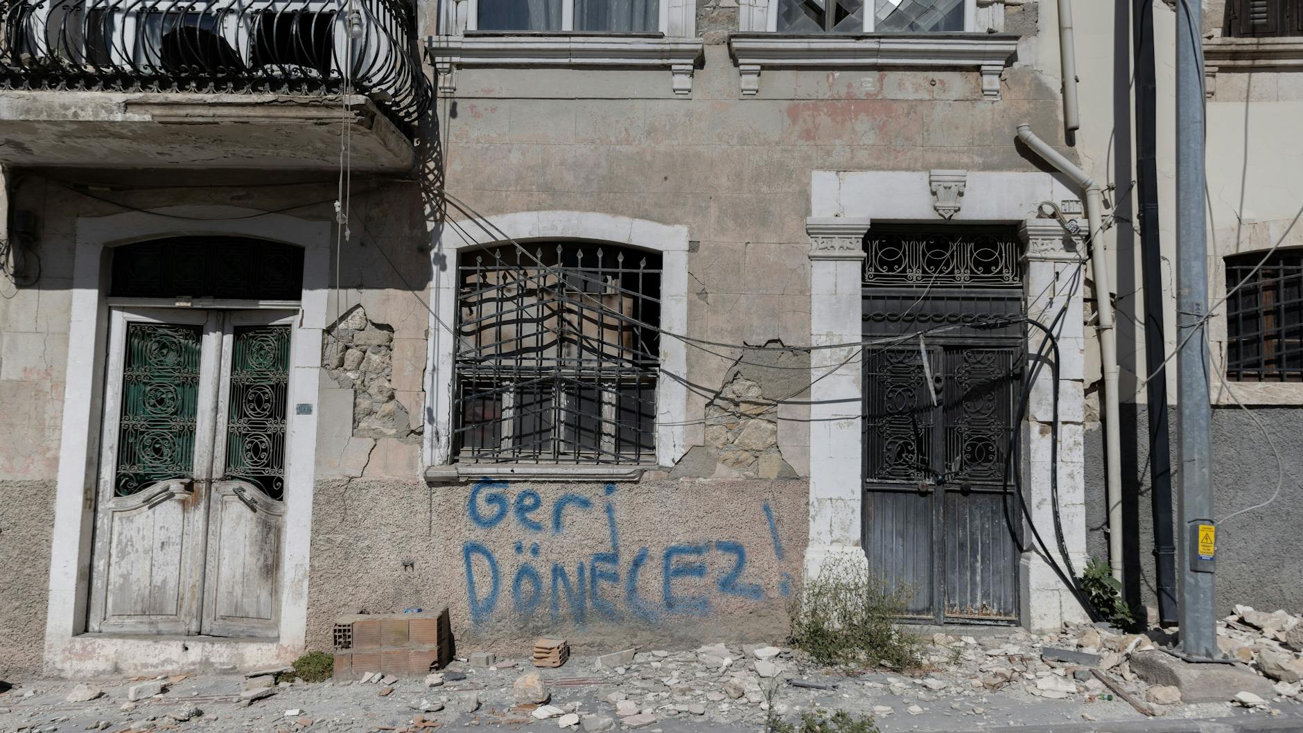„Wir kommen wieder“ steht an der Wand eines Hauses, vor dem noch Trümmer des Erdbebens liegen.